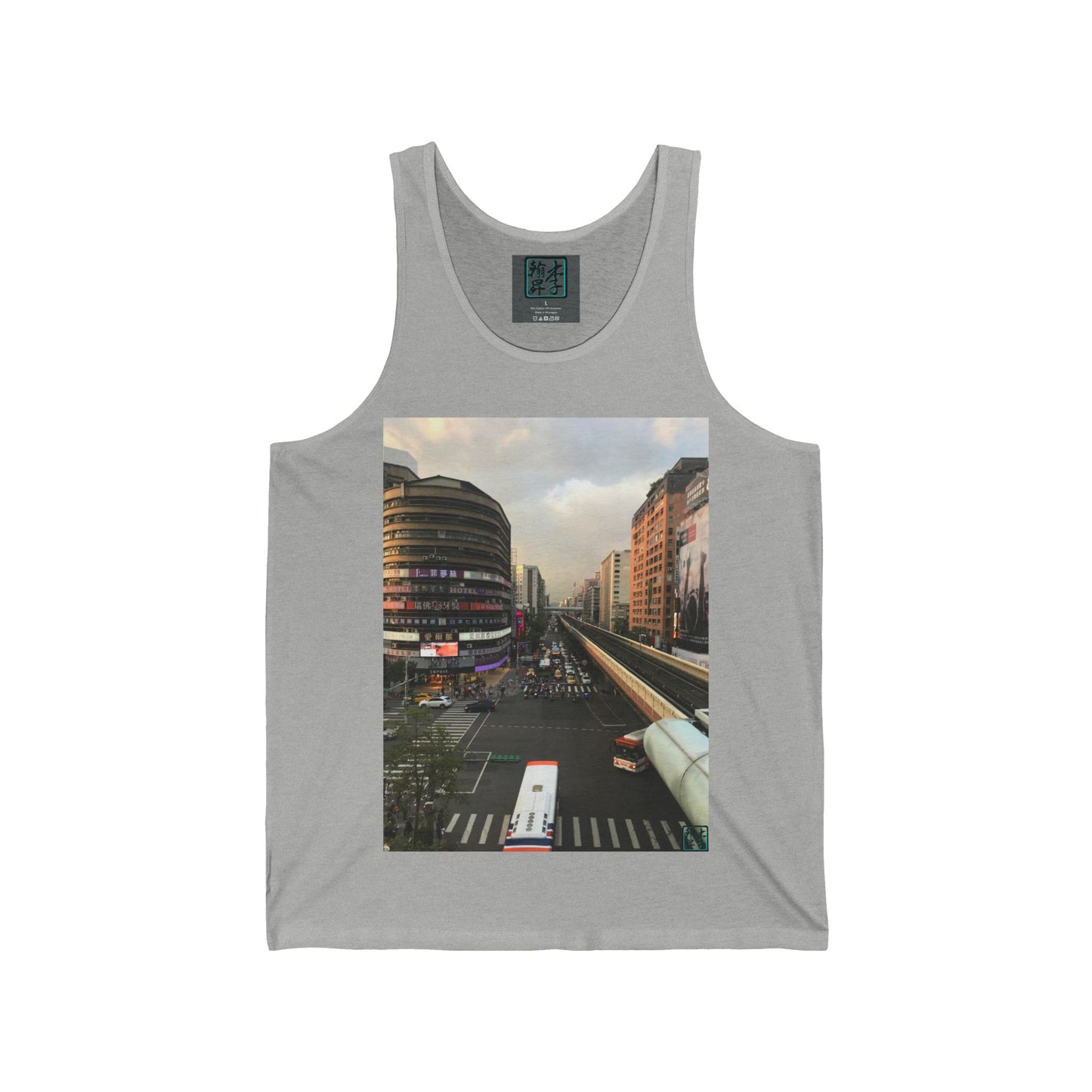 This is the Athletic Heather Taipei MRT Sunset Tank by Lee Hansheng Studios.This showcases the front of the tank.It is a rectangular image of Taipei.Circular brown building to the left,rectangular brown and white buildings to the right,two white/red buses pulling onto the road,overcast white,light red and grey skies,some trees to the right.It is the overall scenery from the looking across the road at higher ground.The studio logo on in the side of shirt,on top of gray label,size label is in white.