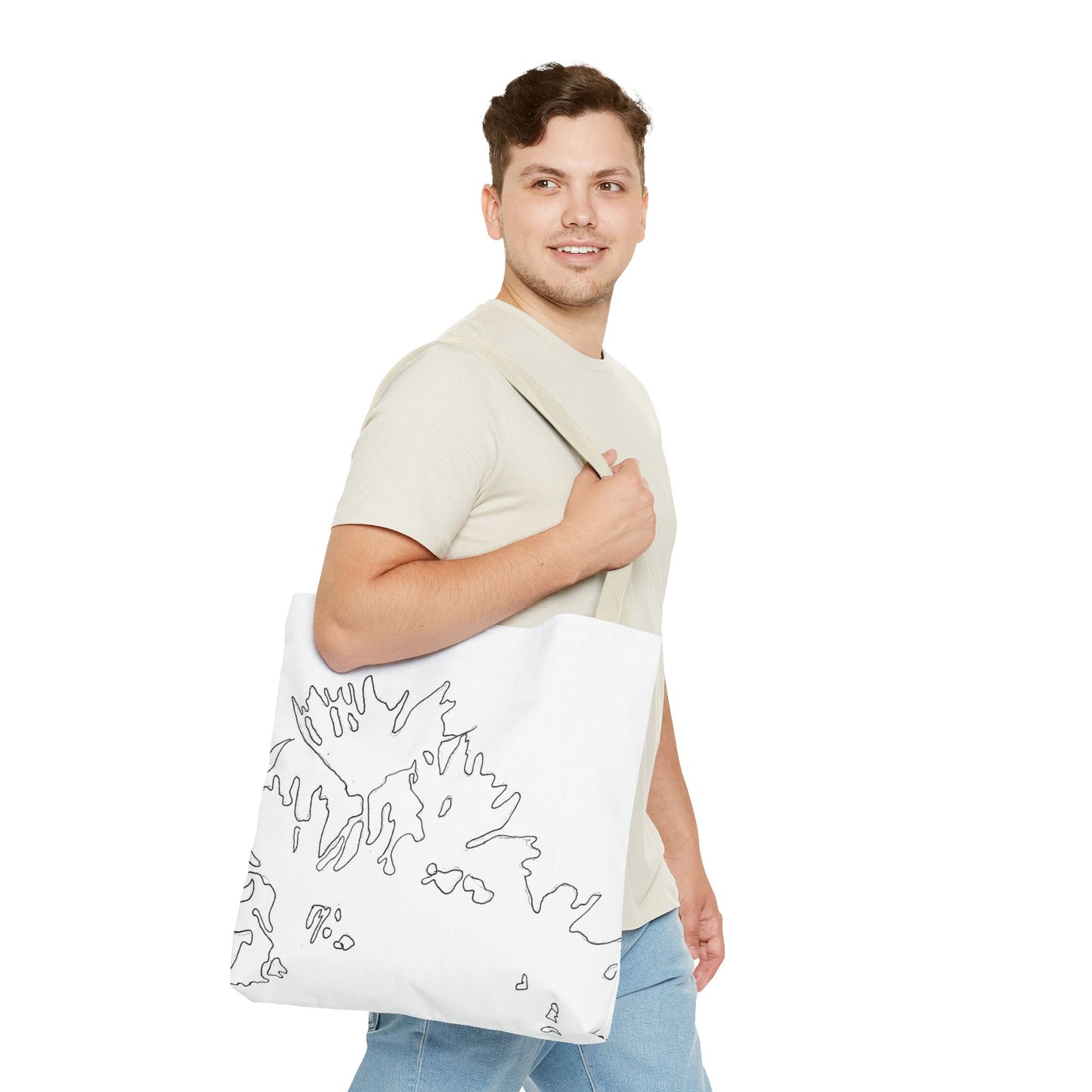 This is the Beige 18" x 18" Flowers Tote Bag by Storm Garden Studio. The tote has color matched straps, abstract line work which is outlines of flowers, all over print. The colors are white and black. A brunette man is walking towards the right wearing the white tee and light jeans. He is looking towards the left and smiling with the tote over his shoulder, hand holding the handles. He is against a white background.