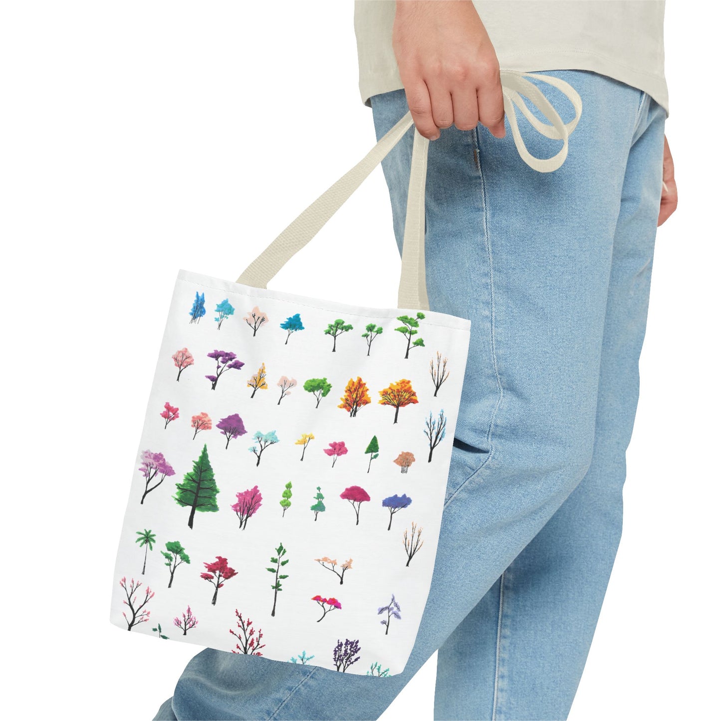 The Beige 13" x 13" Study of Trees Tote with color matched handles by Lee Hansheng Studios. There are a variety of tree illustrations from blooming fruit trees to deciduous and evergreens. The trees are colored pinks, purples, greens, yellows, blues and oranges on a white background tote. A man's hand with a beige tee and light- colored jeans is grabbing the handles from the hip down. The tote is against a white background.