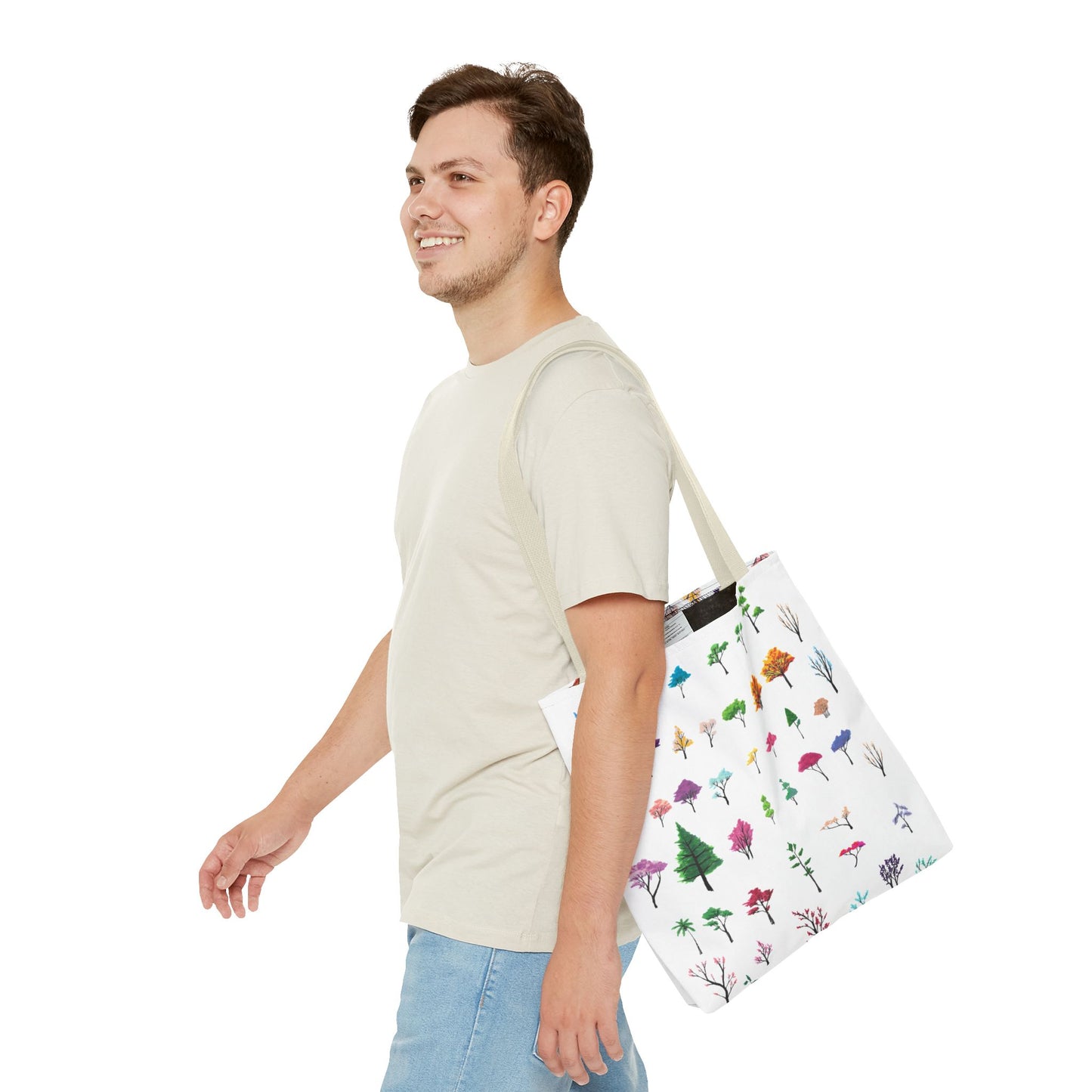 The Beige 13" x 13" Study of Trees Tote with color matched handles by Lee Hansheng Studios. There are a variety of tree illustrations from blooming fruit trees to deciduous and evergreens. The trees are colored pinks, purples, greens, yellows, blues and oranges on a white background. A man with a smile, short wavy brown hair, beige tee plus jeans with tote around their shoulder and walking towards the left against a white background.