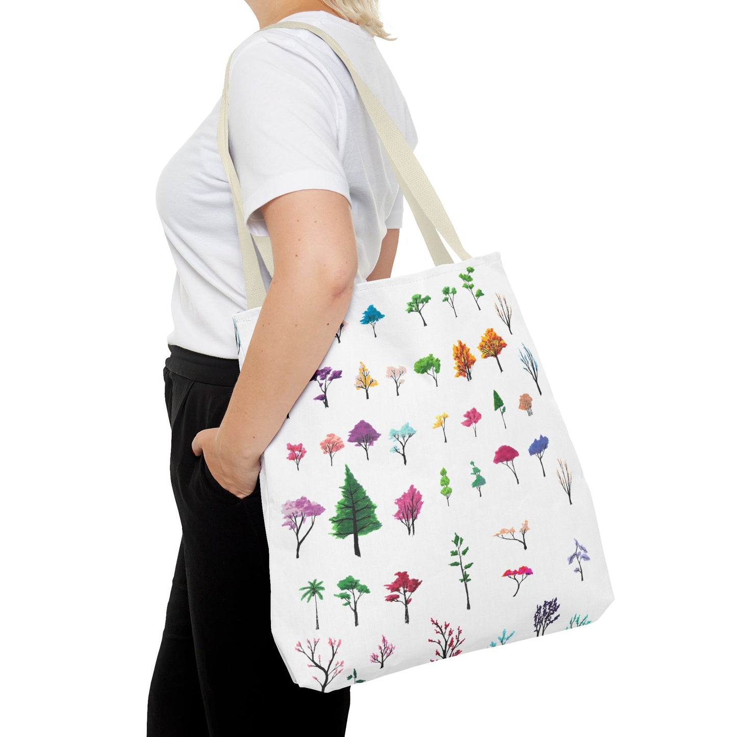 This is the Beige 18" x 18" Study of Trees Tote with color matched handles by Lee Hansheng Studios. There are a variety of tree illustrations from blooming fruit trees to deciduous and evergreens. The trees are colored pinks, purples, greens, yellows, blues and oranges on a white background. The tote is over the shoulder of a short blonde haired woman who has a white tee and black pants. Her hand is in the pocket of the pants and image only shows from the neck to upper thigh.