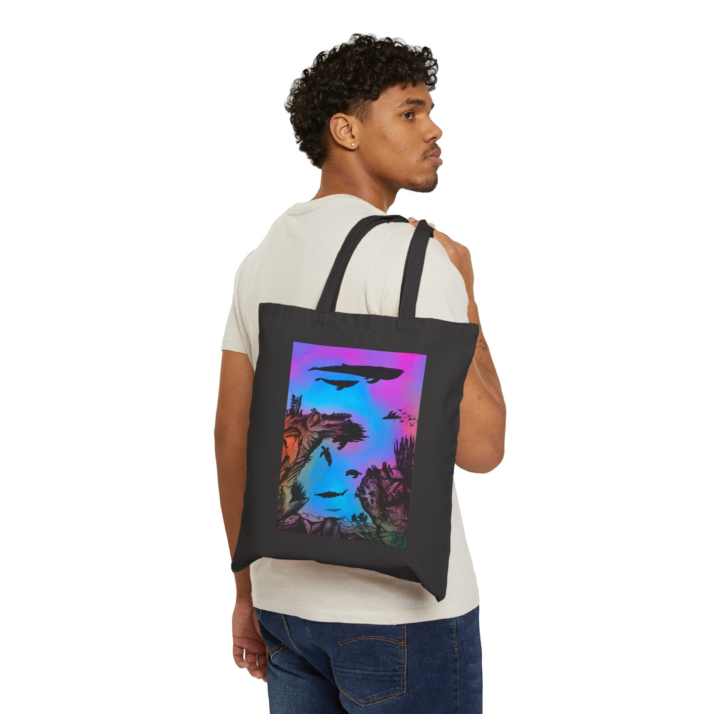 This is the Black 15" x 16" Into the Abyss Canvas Tote by Lee Hansheng Studios. The underwater seascape with aquatic plants on a marbled background.Two blue whales,1 goblin shark,school of eagle rays,two sea turtles and a school of fish.On the bottom right corner is the studio logo printed in black outlined in blue.The colors are pink,purple,blue and red/orange.A man looking to the right is holding the handles with the tote over his shoulder showing the front and wearing a white tee and dark jeans.