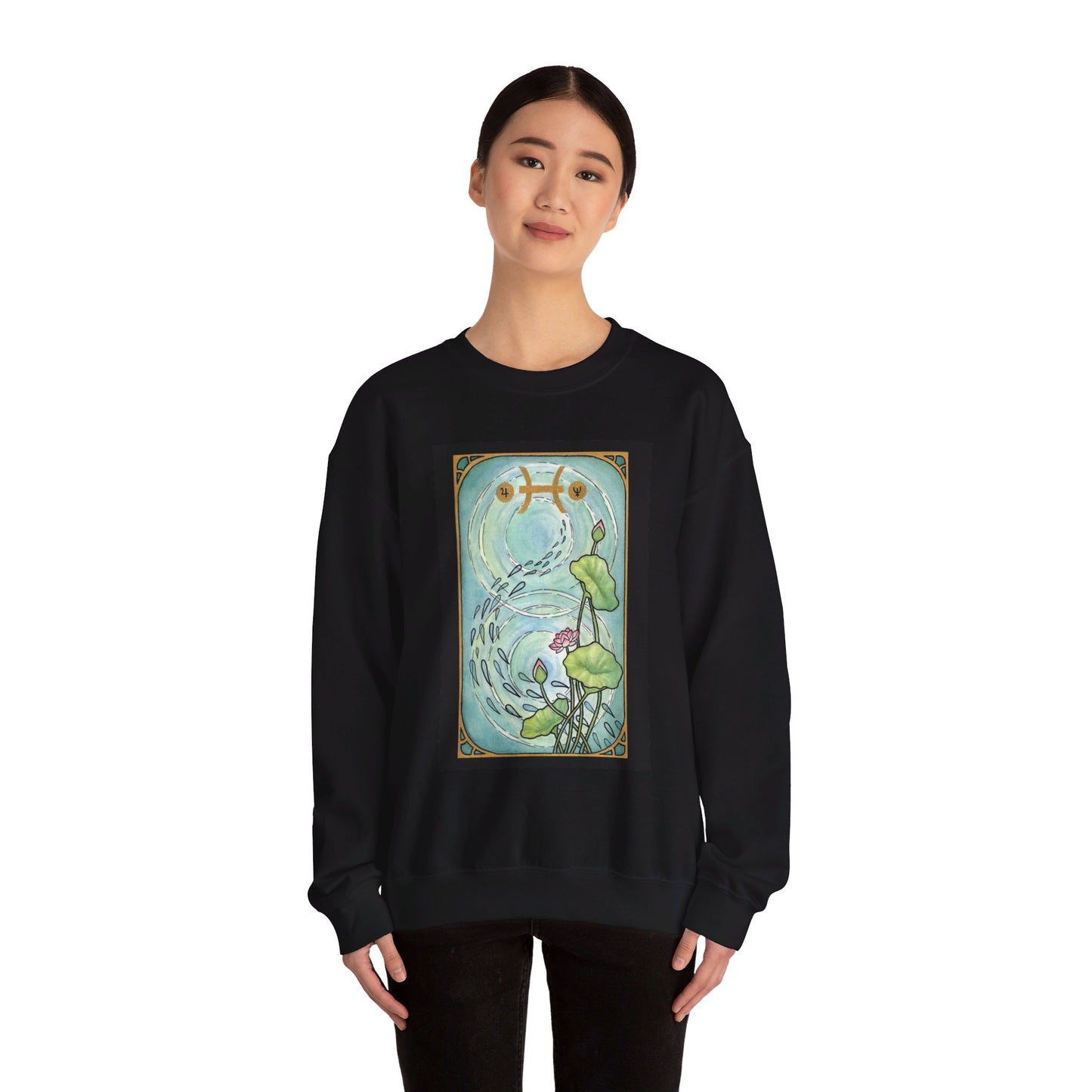 This is the Black Pisces Sweatshirt by Chris Foster Design that comes in sizes S-3XL and illustration starts from the upper chest till below the belly button. Designed like a tarot card with gold border and pisces symbol. In the background a pond that has two circular ripples, the right side has the lily flowers with two green leaves, one blooming pink flower, two buds, and a green trail of seeds. A lady with a smile, black pants, hair tied and hands to the sides is wearing the sweatshirt.