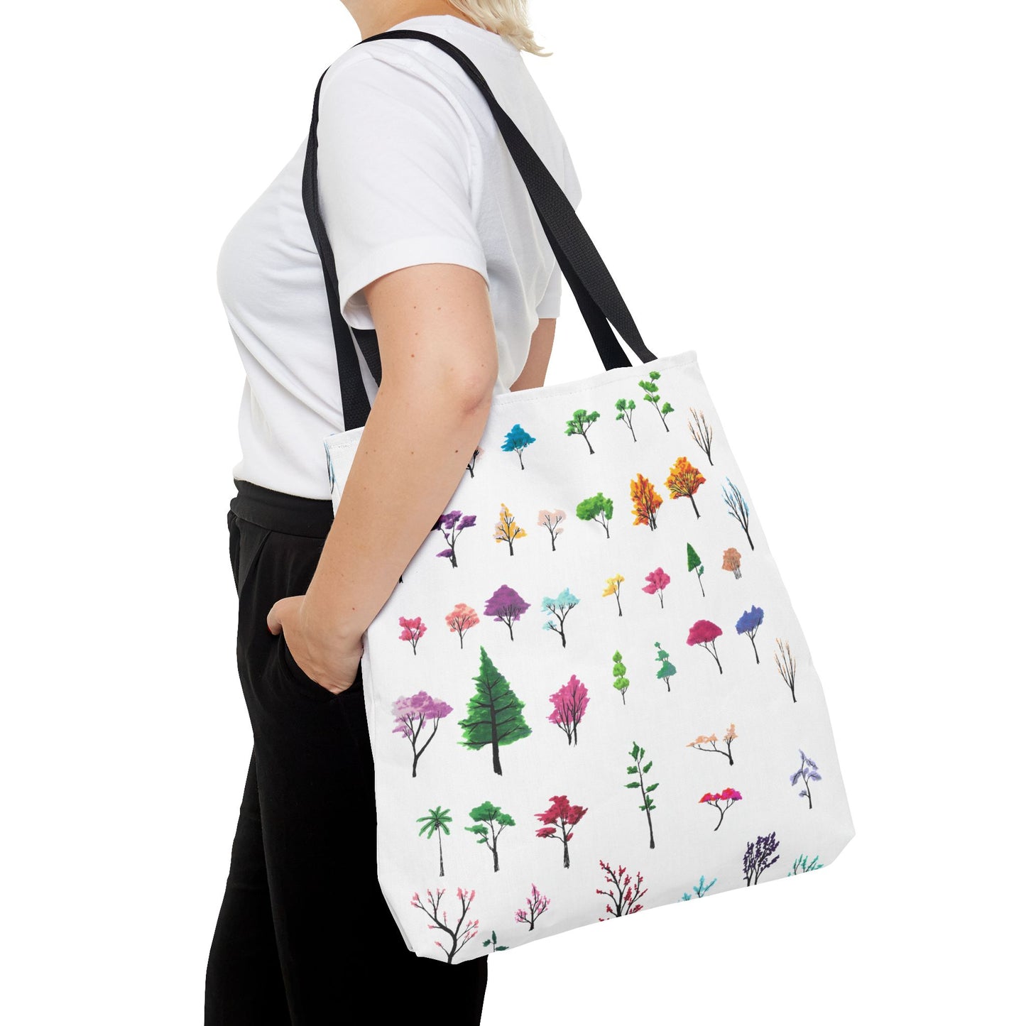This is the Black 18" x 18" Study of Trees Tote with color matched handles by Lee Hansheng Studios. There are a variety of tree illustrations from blooming fruit trees to deciduous and evergreens. The trees are colored pinks, purples, greens, yellows, blues and oranges on a white background. The tote is over the shoulder of a short blonde haired woman who has a white tee and black pants. Her hand is in the pocket of the pants and image only shows from the neck to upper thigh.
