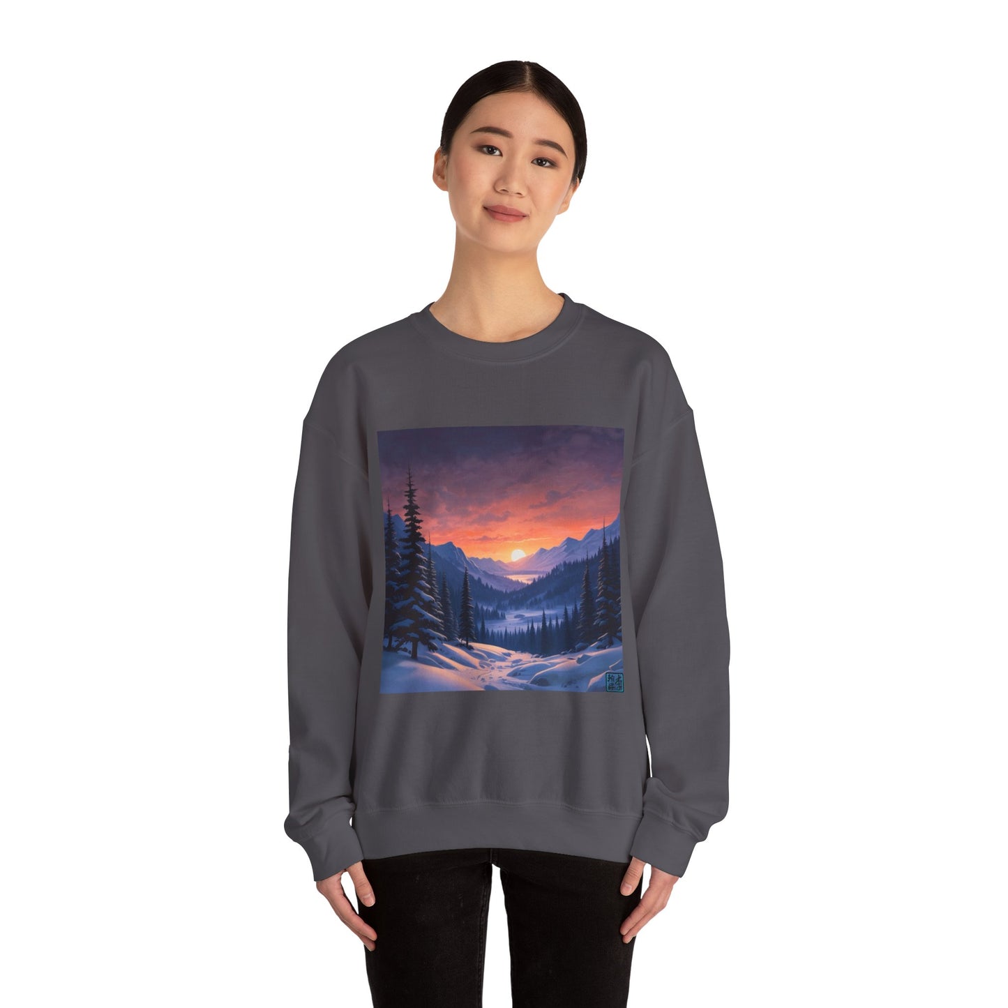 This is the Charcoal Snow Valley Sweatshirt that is a crewneck coming in S - 5XL sizes. It is worn by an Asian lady who has black hair tied in a bun, black pants and is standing against a white background with a smile. This design is by Lee Hansheng Studios and showcases a snowy hill/mountain area with large pine trees on both sides continuing into the horizon. The sun is rising past the horizon and consist of yellow, orange, red hues which is illuminated onto the clouds, snowy field, mountains and trees.