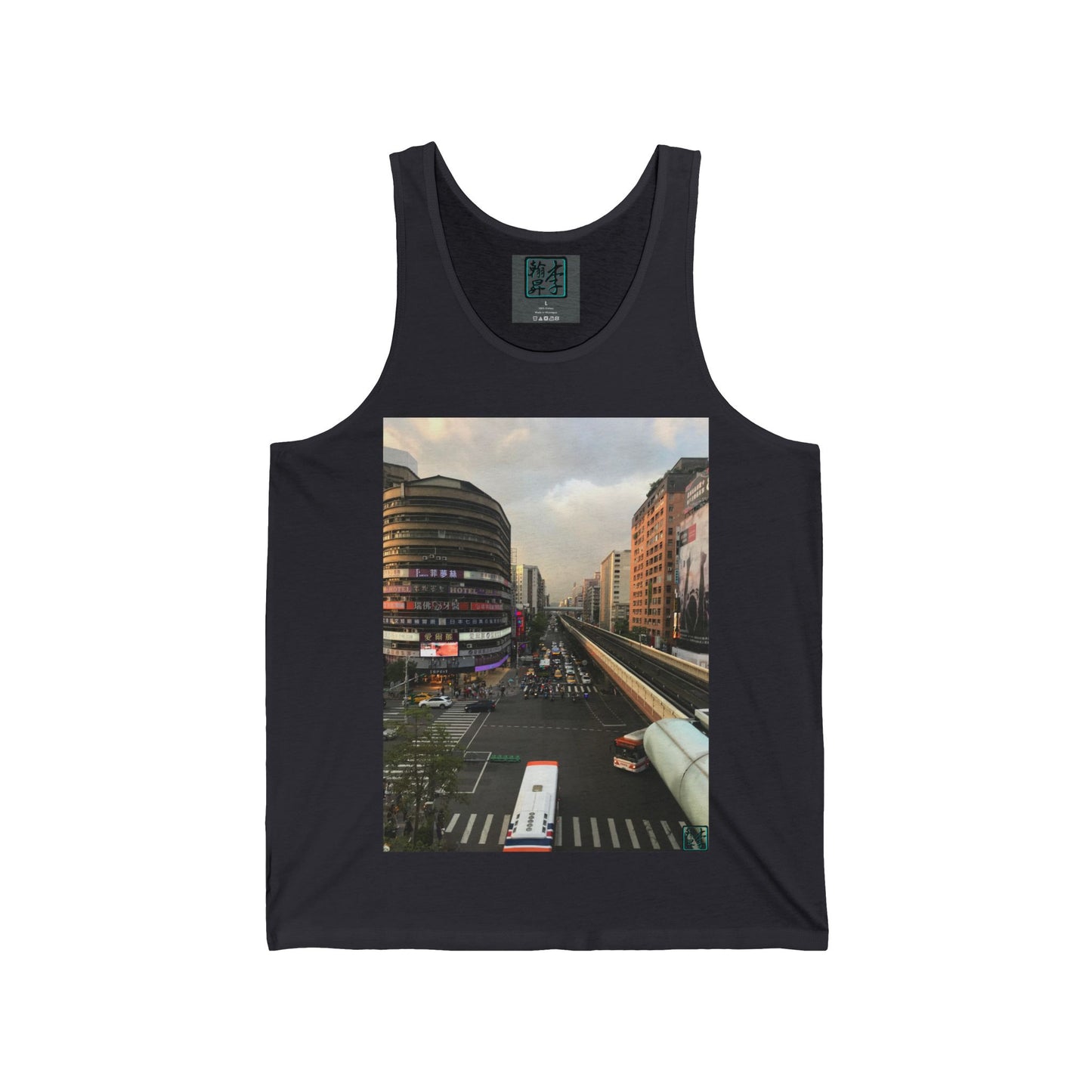 This is the Dark Grey Taipei MRT Sunset Tank by Lee Hansheng Studios.This showcases the front of the tank.It is a rectangular image of Taipei.Circular brown building to the left,rectangular brown and white buildings to the right,two white/red buses pulling onto the road,overcast white,light red and grey skies,some trees to the right.It is the overall scenery from the looking across the road at higher ground.The studio logo on in the side of shirt,on top of gray label,size label is in white.