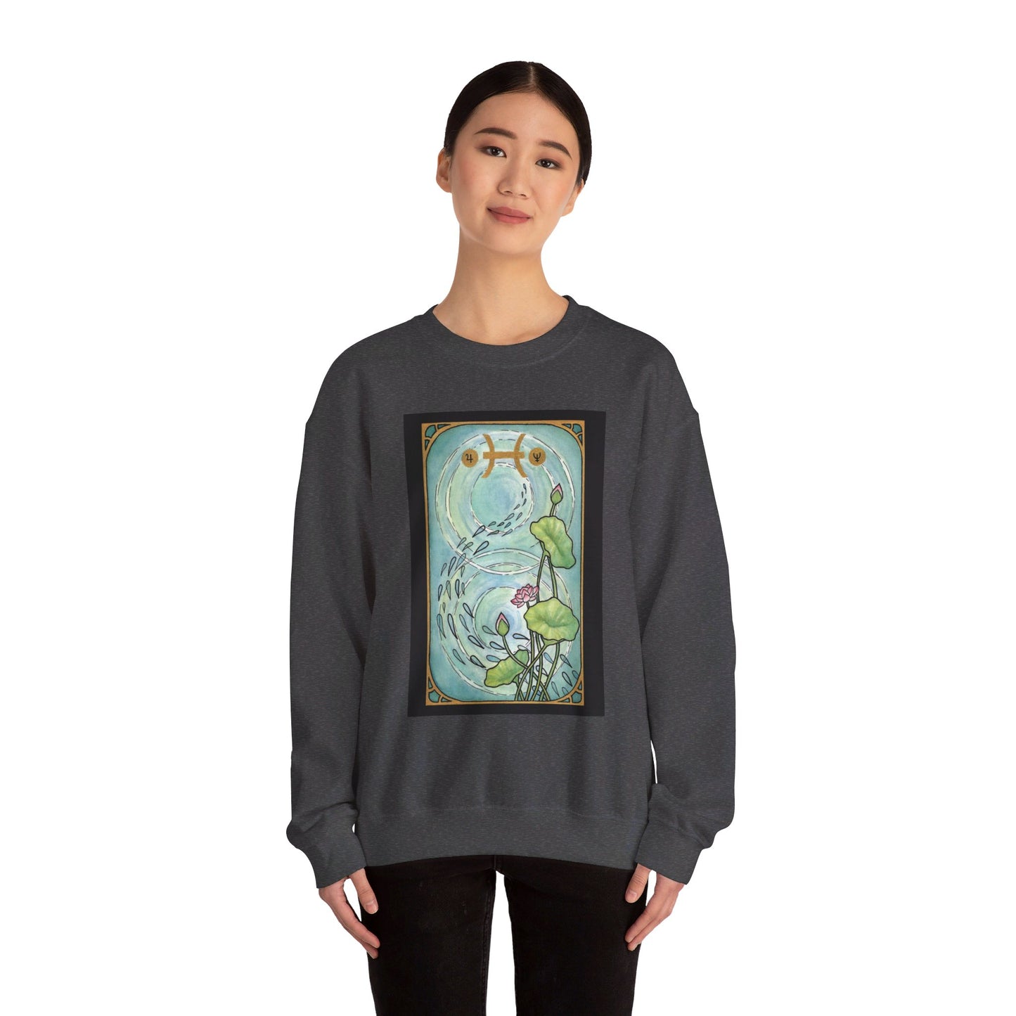 This is the Dark Heather Pisces Sweatshirt by Chris Foster Design that comes in sizes S-3XL and illustration starts from the upper chest till below the belly button. Designed like a tarot card with gold border and pisces symbol. In the background a pond that has two circular ripples, the right side has the lily flowers with two green leaves, one blooming pink flower, two buds, and a green trail of seeds. A lady with a smile, black pants, hair tied and hands to the sides is wearing the sweatshirt.