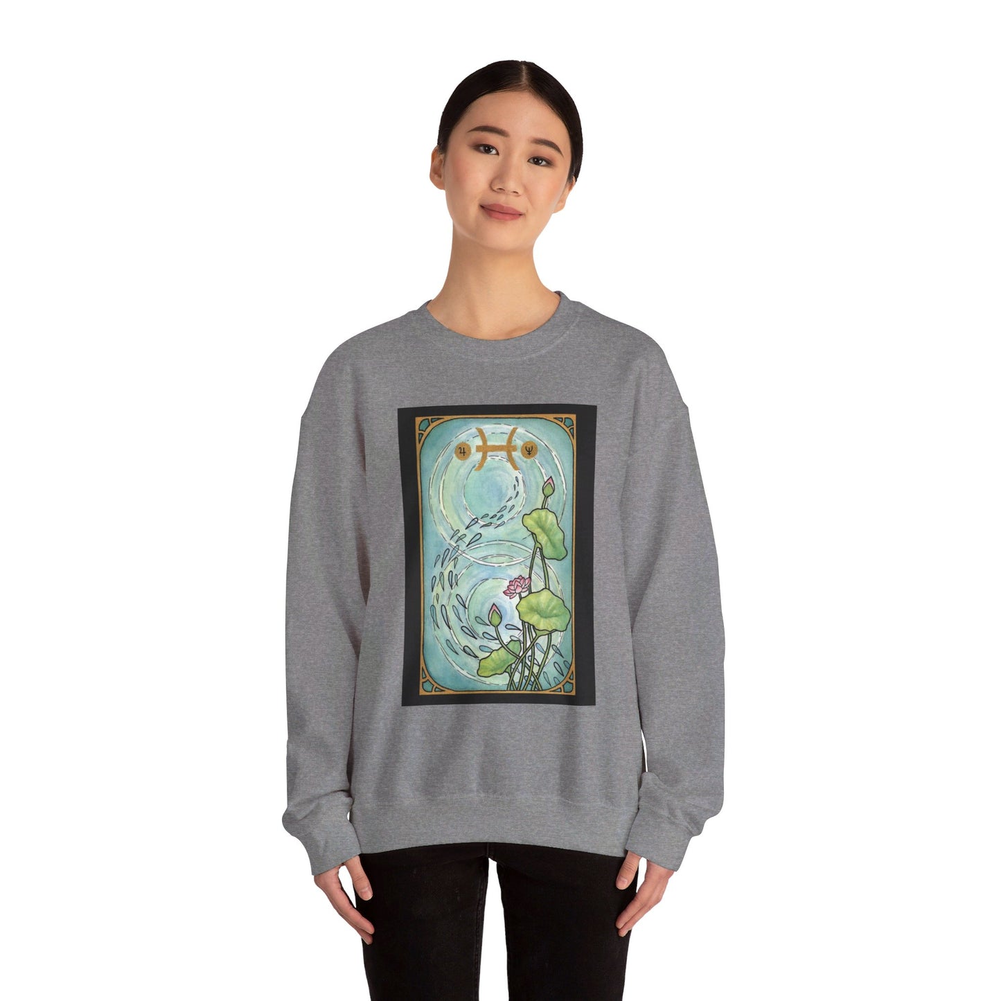 This is the Graphite Heather Pisces Sweatshirt by Chris Foster Design that comes in sizes S-3XL and illustration starts from the upper chest till below the belly button. Designed like a tarot card with gold border and pisces symbol. In the background a pond that has two circular ripples, the right side has the lily flowers with two green leaves, one blooming pink flower, two buds, and a green trail of seeds. A lady with a smile, black pants, hair tied and hands to the sides is wearing the sweatshirt.