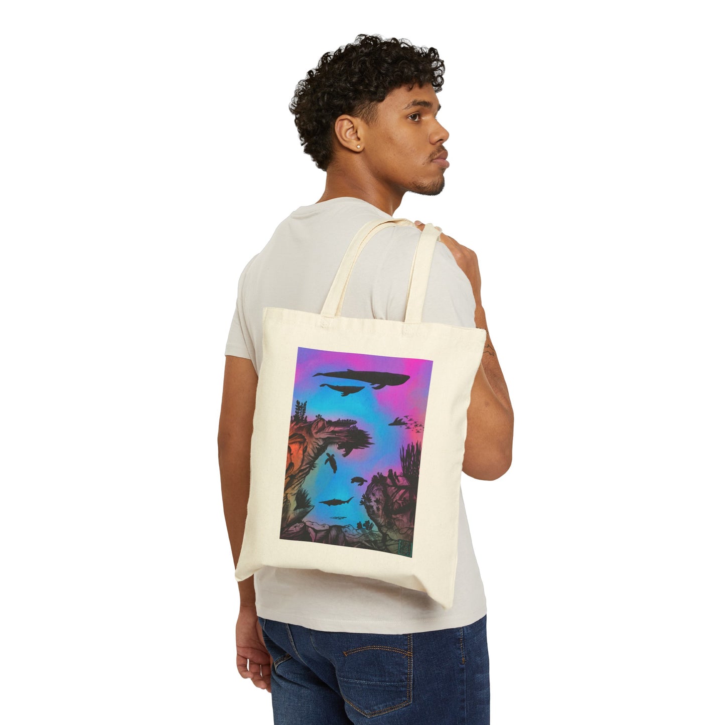 This is the Natural 15" x 16" Into the Abyss Canvas Tote by Lee Hansheng Studios. The underwater seascape with aquatic plants on a marbled background.Two blue whales,1 goblin shark,school of eagle rays,two sea turtles and a school of fish.On the bottom right corner is the studio logo printed in black outlined in blue.The colors are pink,purple,blue and red/orange.A man looking to the right is holding the handles with the tote over his shoulder showing the front and wearing a white tee and dark jeans.