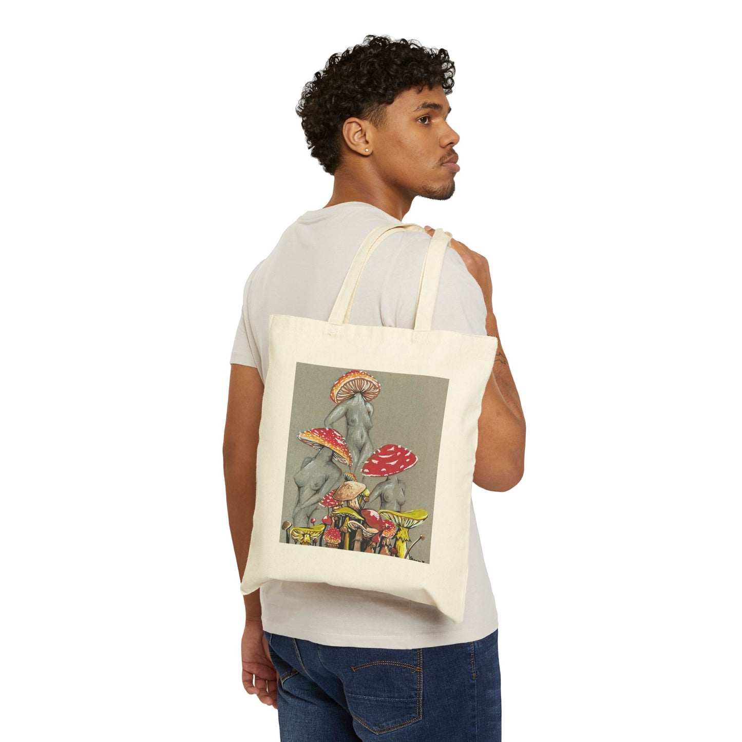 This is the Natural 15" x 16" Miss Amanita Cotton Canvas Tote Bag by Storm Garden Studio. This is an illustration of three mushroom headed nude women. The foreground has assorted mushrooms in different sizes. The women are positioned in a triangle shape. The colors range from yellow, orange and red. Each of the bodies are shaded in white, black or grey and match the background of the illustration. A man is hanging the tote over his shoulder looking to the right with a white tee and dark jeans.