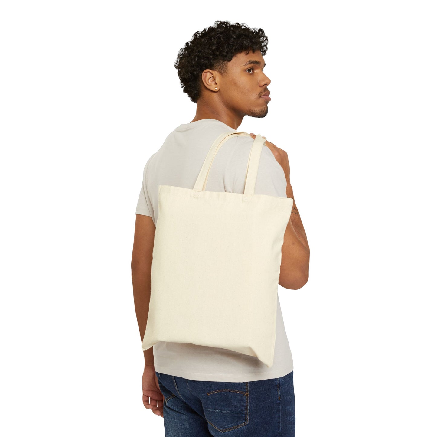 This is the Natural 15" x 16" Miss Amanita Cotton Canvas Tote Bag by Storm Garden Studio. This is the back of the tote and is the color of the tote. There is no illustration on this side. A man is hanging the tote over his shoulder looking to the right with a white tee and dark jeans against a white background.