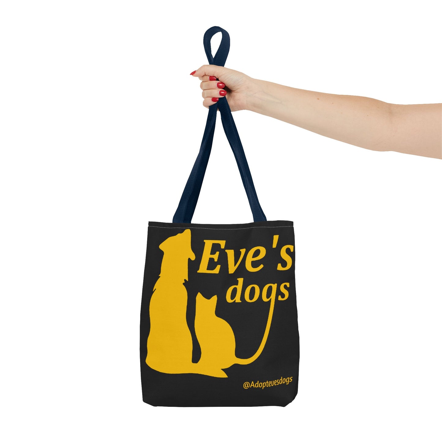 This is the Navy 16" x 16" Adopt Eve's Dog Tote Bag. The handles are navy. The top of the tote is hemmed in yellow. The tote is all over black with the image of a dog, cat, "Eve's Dogs" and "@Adoptevesdogs" in yellow. A woman's hand with red nail polish is grabbing the handles. Her arm is outstretched to the middle. The tote is against a white background.