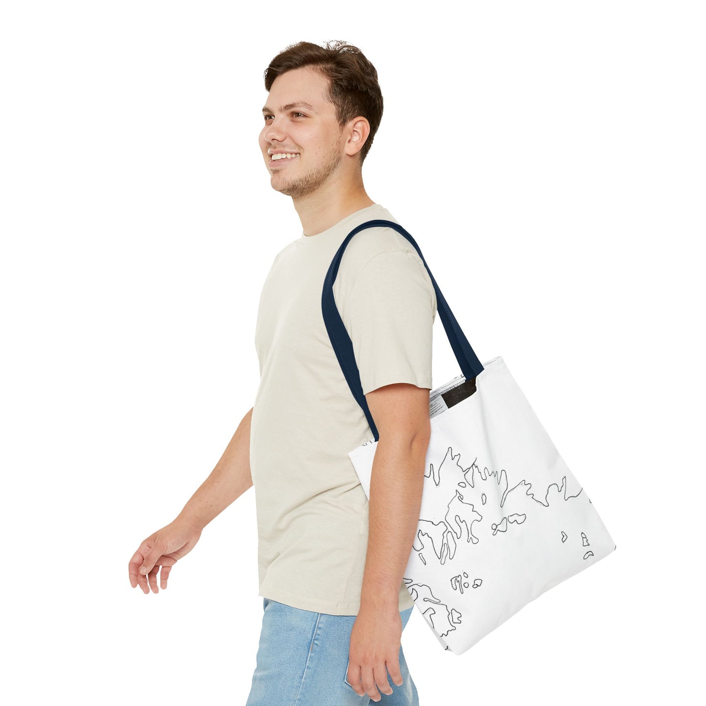 This is the Navy 13" x 13" Flowers Tote Bag by Storm Garden Studio. The tote has color matched straps, abstract line work which is outlines of flowers, all over print. The colors are white and black. A brunette man is walking towards the left wearing the white tee and light jeans. He is looking towards the left and smiling with the tote over his shoulder. He is against a white background.