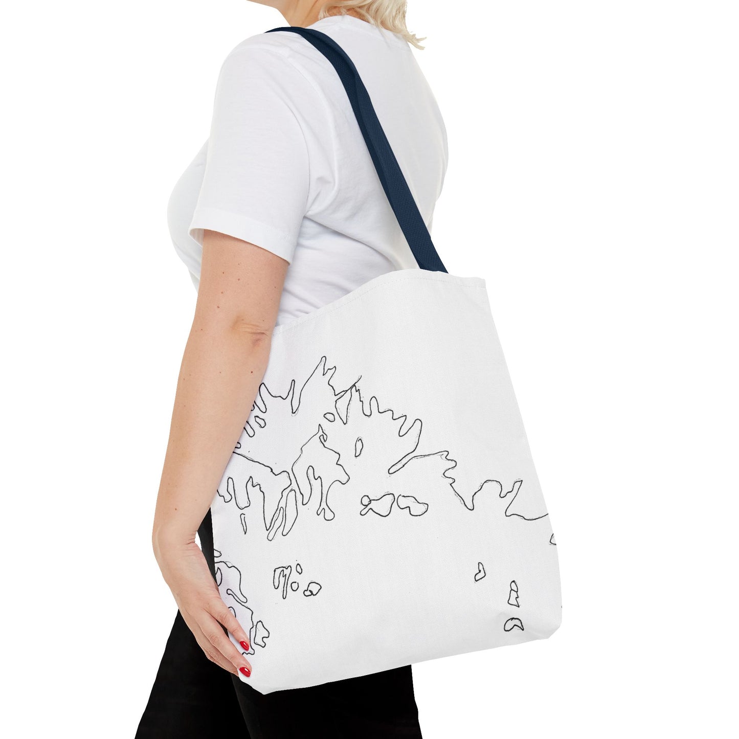 This is the Navy 16" x 16" Flowers Tote Bag by Storm Garden Studio. The tote has color matched straps, abstract line work which is outlines of flowers, all over print. The colors are white and black. A blond haired lady is walking towards the left wearing a white tee, black pants, hand on tote bag and image is from the shoulders down. She is against a white background.