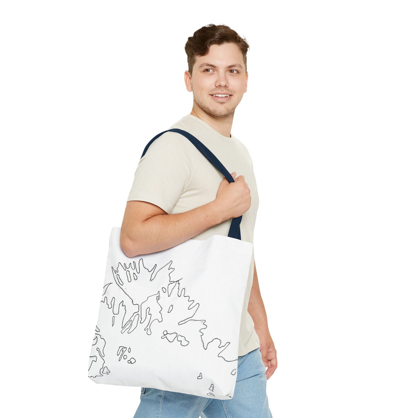 This is the Navy 18" x 18" Flowers Tote Bag by Storm Garden Studio. The tote has color matched straps, abstract line work which is outlines of flowers, all over print. The colors are white and black. A brunette man is walking towards the right wearing the white tee and light jeans. He is looking towards the left and smiling with the tote over his shoulder, hand holding the handles. He is against a white background.