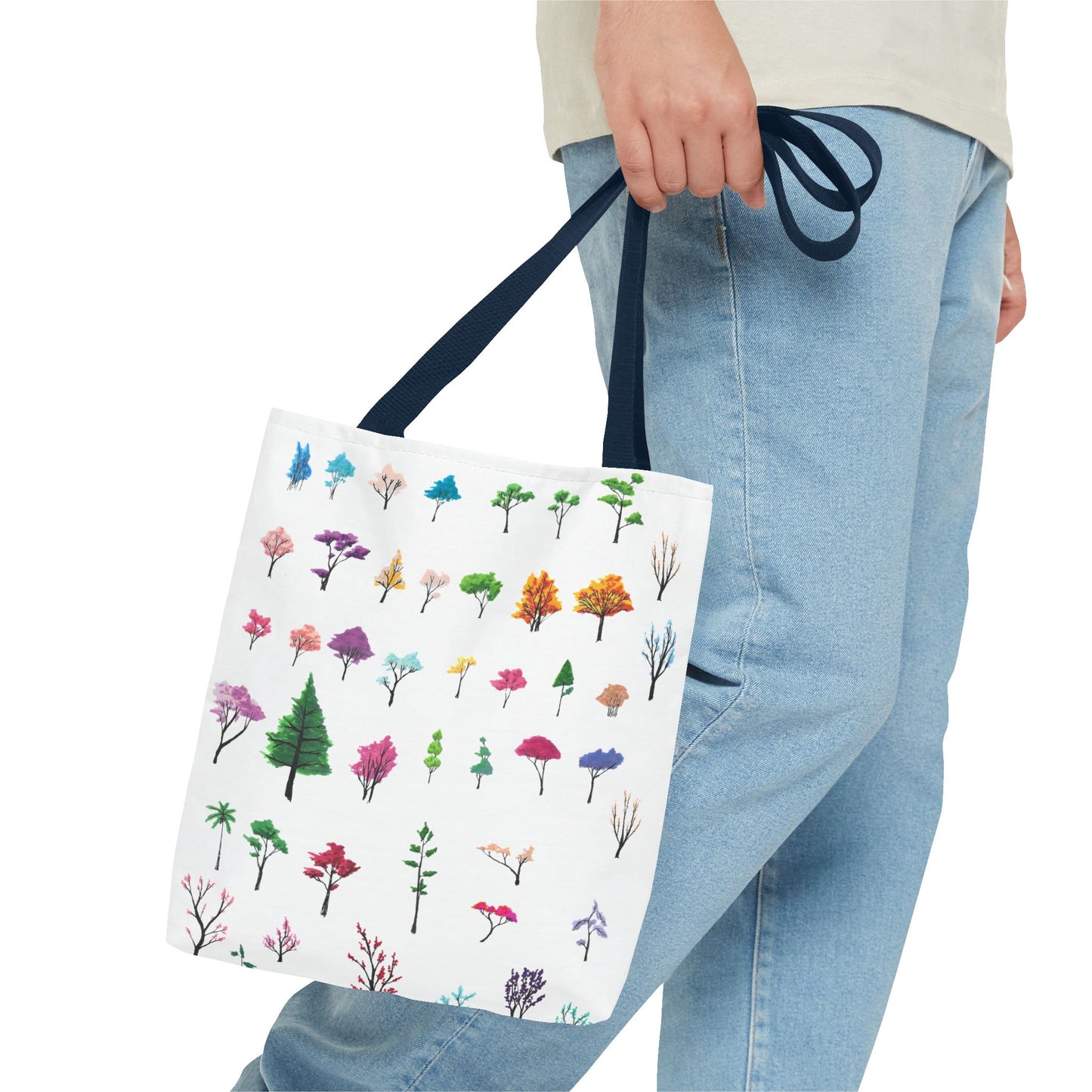 The Navy 13" x 13" Study of Trees Tote with color matched handles by Lee Hansheng Studios. There are a variety of tree illustrations from blooming fruit trees to deciduous and evergreens. The trees are colored pinks, purples, greens, yellows, blues and oranges on a white background tote. A man's hand with a beige tee and light- colored jeans is grabbing the handles from the hip down. The tote is against a white background.