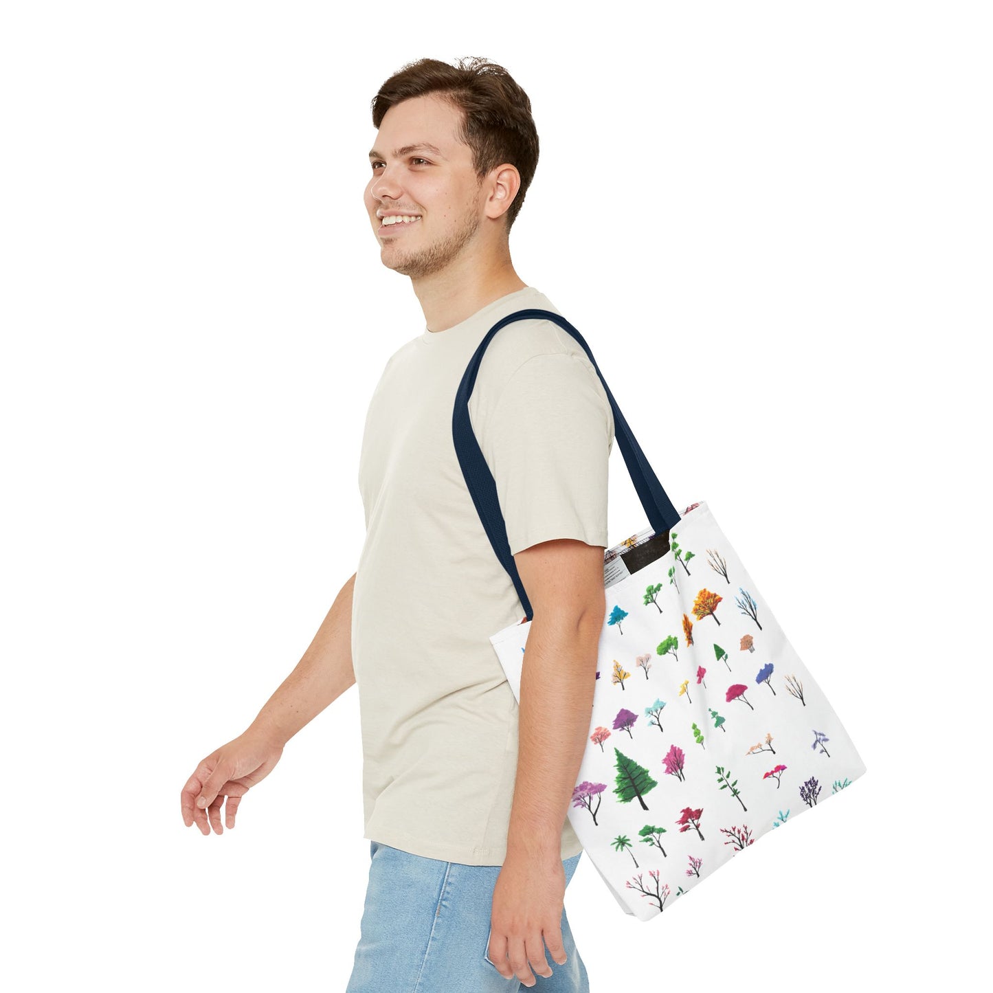 The Navy 13" x 13" Study of Trees Tote with color matched handles by Lee Hansheng Studios. There are a variety of tree illustrations from blooming fruit trees to deciduous and evergreens. The trees are colored pinks, purples, greens, yellows, blues and oranges on a white background. A man with a smile, short wavy brown hair, beige tee plus jeans with tote around their shoulder and walking towards the left against a white background.