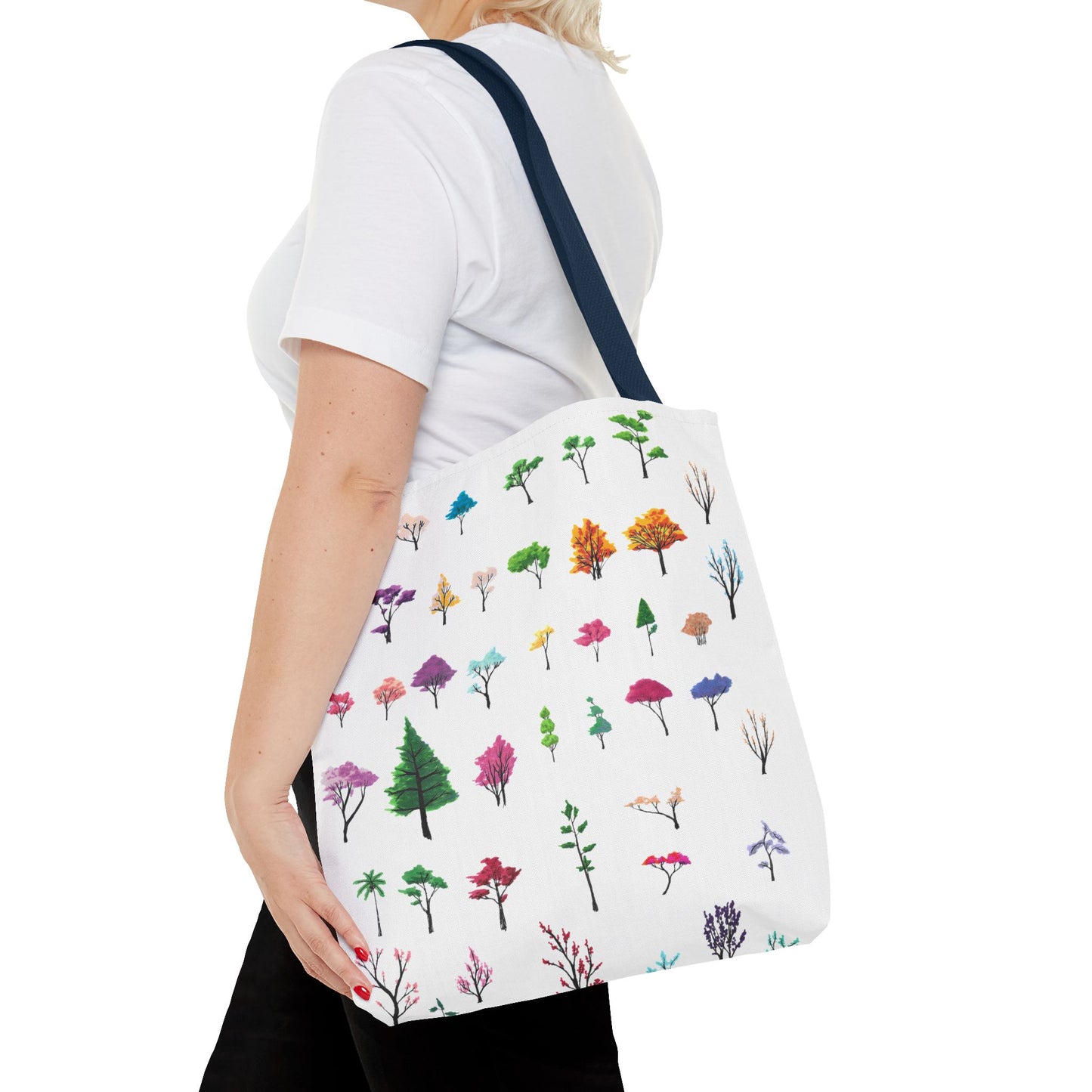 This is the Navy 16" x 16" Study of Trees Tote with color matched handles by Lee Hansheng Studios. There are a variety of tree illustrations from blooming fruit trees to deciduous and evergreens. The trees are colored pinks, purples, greens, yellows, blues and oranges on a white background. The tote is over the shoulder of a short blonde haired woman who has a white tee and black pants. Her hand is on the tote and image only shows from the neck to upper thigh.