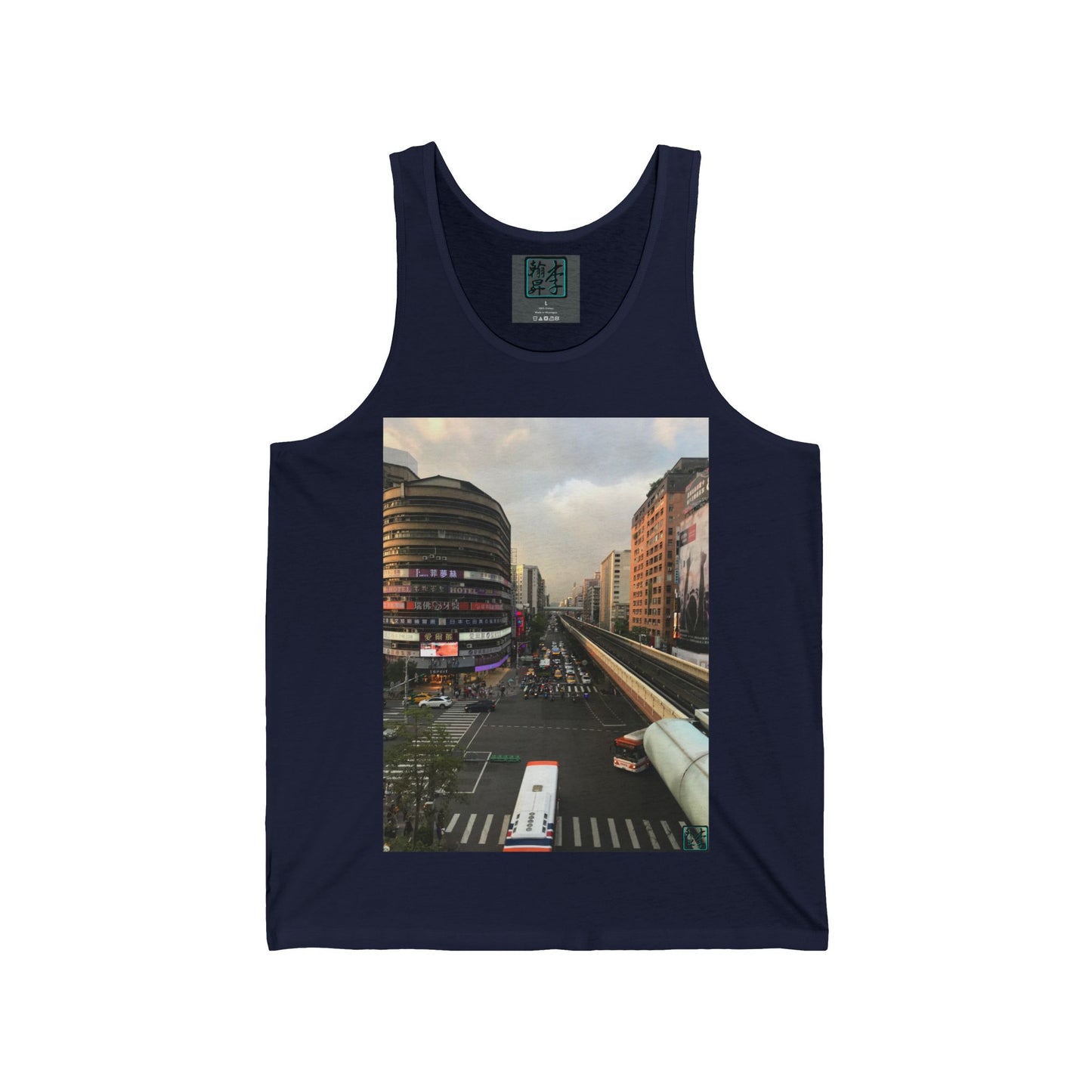 This is the Navy Taipei MRT Sunset Tank by Lee Hansheng Studios. This showcases the front of the tank. It is a rectangular image of Taipei. Circular brown building to the left, rectangular brown and white buildings to the right, two white/red buses pulling onto the road, overcast white, light red and grey skies, some trees to the right. It is the overall scenery from the looking across the road at higher ground. The studio logo on in the side of shirt, on top of gray label, size label is in white.