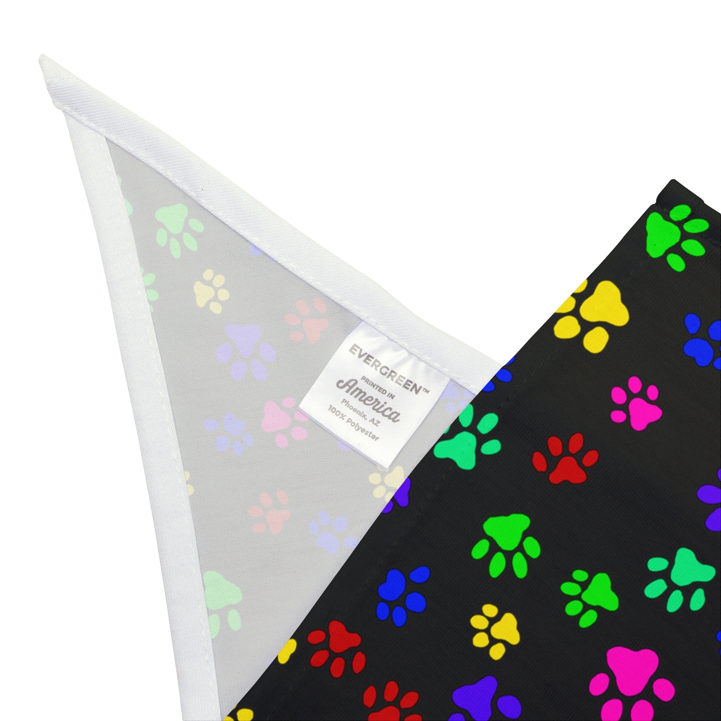 This is the 27" x 13" Paws on Paws Pet Bandana. This shows bandana folded to see the inside. There is a tag showcasing the brand EVERGREEN, printed in America, Phoenix, AZ and 100% polyester. The inside is lined in white and the rest is white. The design shows a triangle shape with different sized color paws on the design. The colors are yellow, green red, blue and purple on a black background.