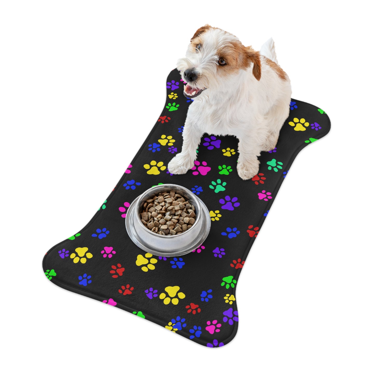 This is the 30" x 18" Bone Shape Paws on Paws Pet Feeding Mat. This shows the bone shape with different sized color paws on the design. The colors are yellow, green red, blue and purple on a black background. There is a white ceramic bowl of food at the middle of one of the sides. The mat is around a white background and you can see the overhead view. A tan and white dog is sitting on the mat with the food in front of it looking to the left.