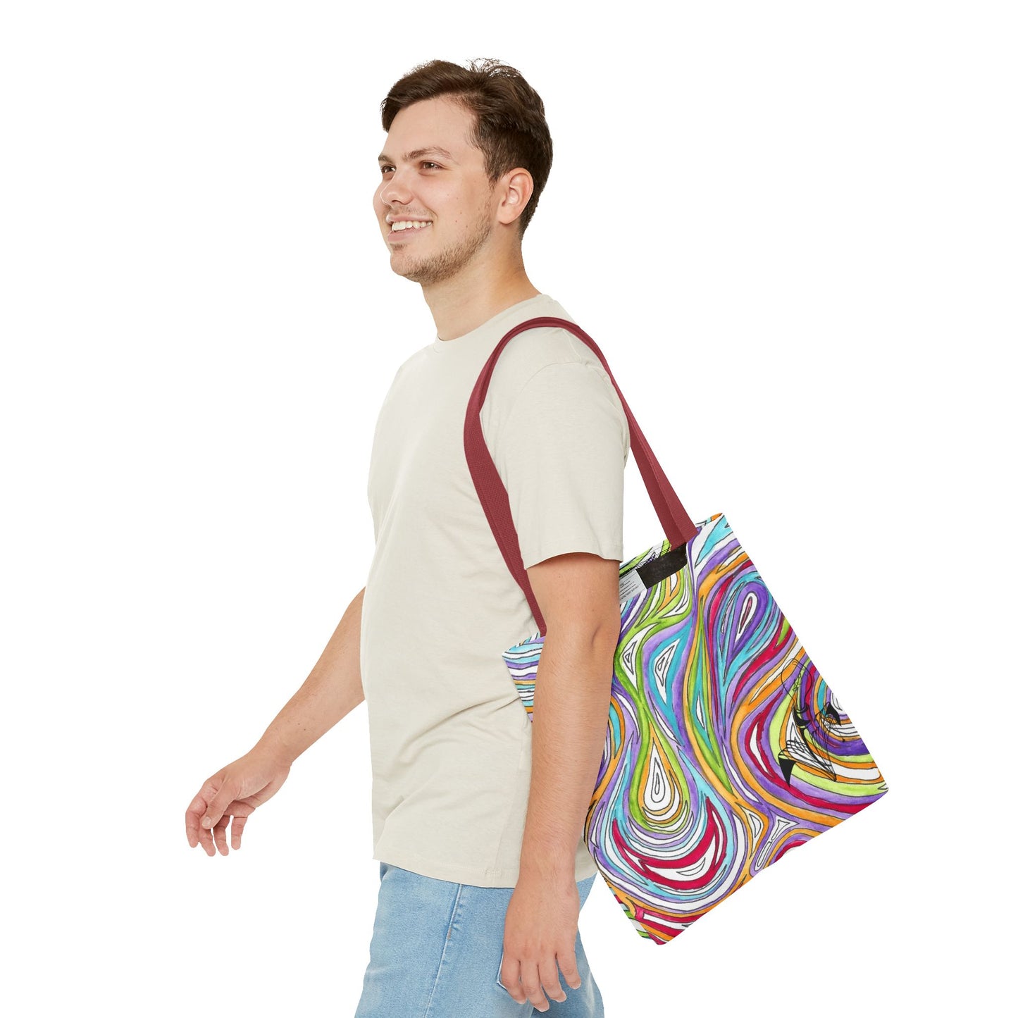 This is the Red 16" x 16" Oil Spill Tote bag by Storm Garden Studios. A smiling brunette man in white shirt, and blue jeans, side view walking to the left carrying the bag with color matched straps, abstract colors and line work, all over print. The colors are lime green, orange, light blue, dark red, purple, white and black. Storm Garden Studio logo printed in black on bottom right of tote bag. He is against a white background.