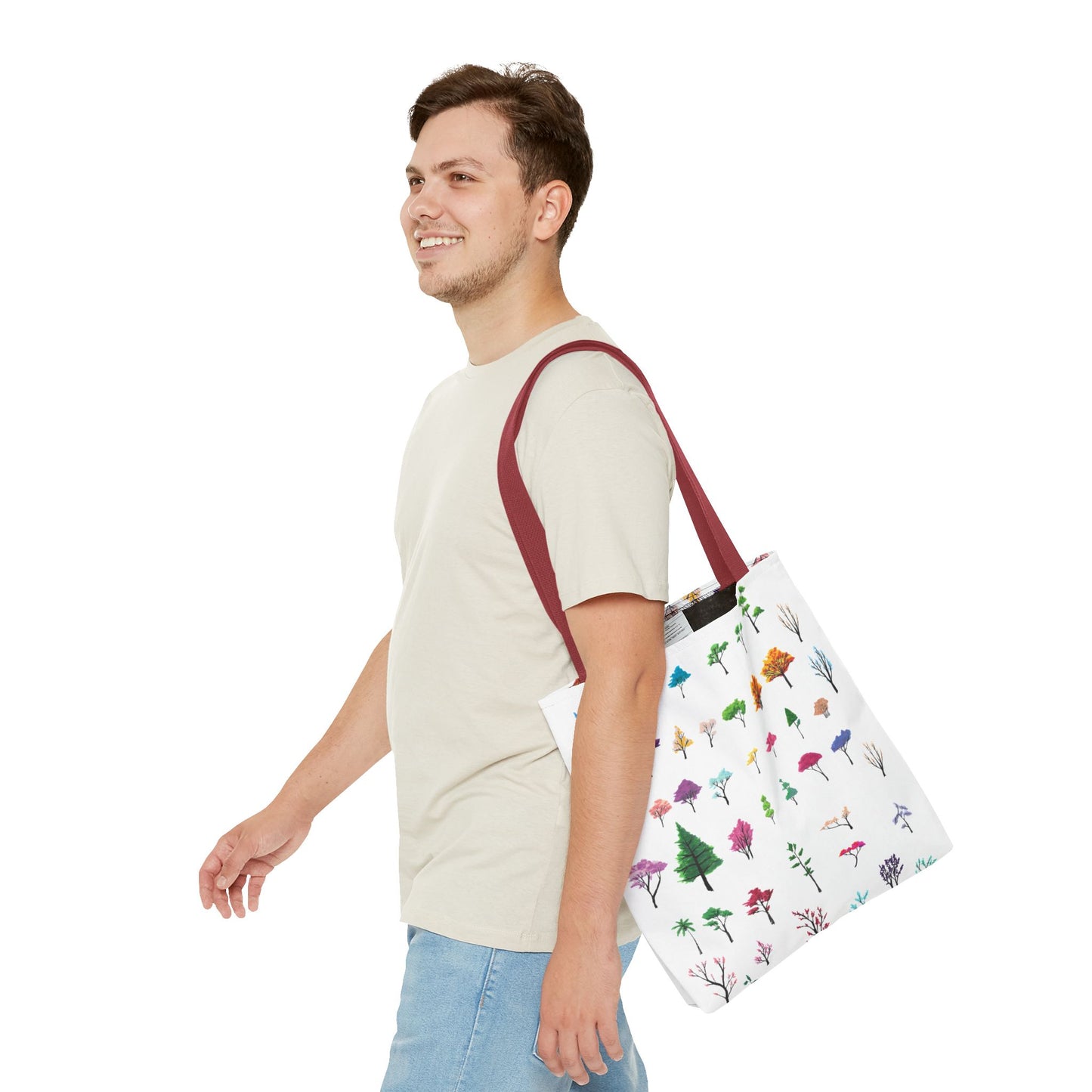 The Red 13" x 13" Study of Trees Tote with color matched handles by Lee Hansheng Studios. There are a variety of tree illustrations from blooming fruit trees to deciduous and evergreens. The trees are colored pinks, purples, greens, yellows, blues and oranges on a white background. A man with a smile, short wavy brown hair, beige tee plus jeans with tote around their shoulder and walking towards the left against a white background.