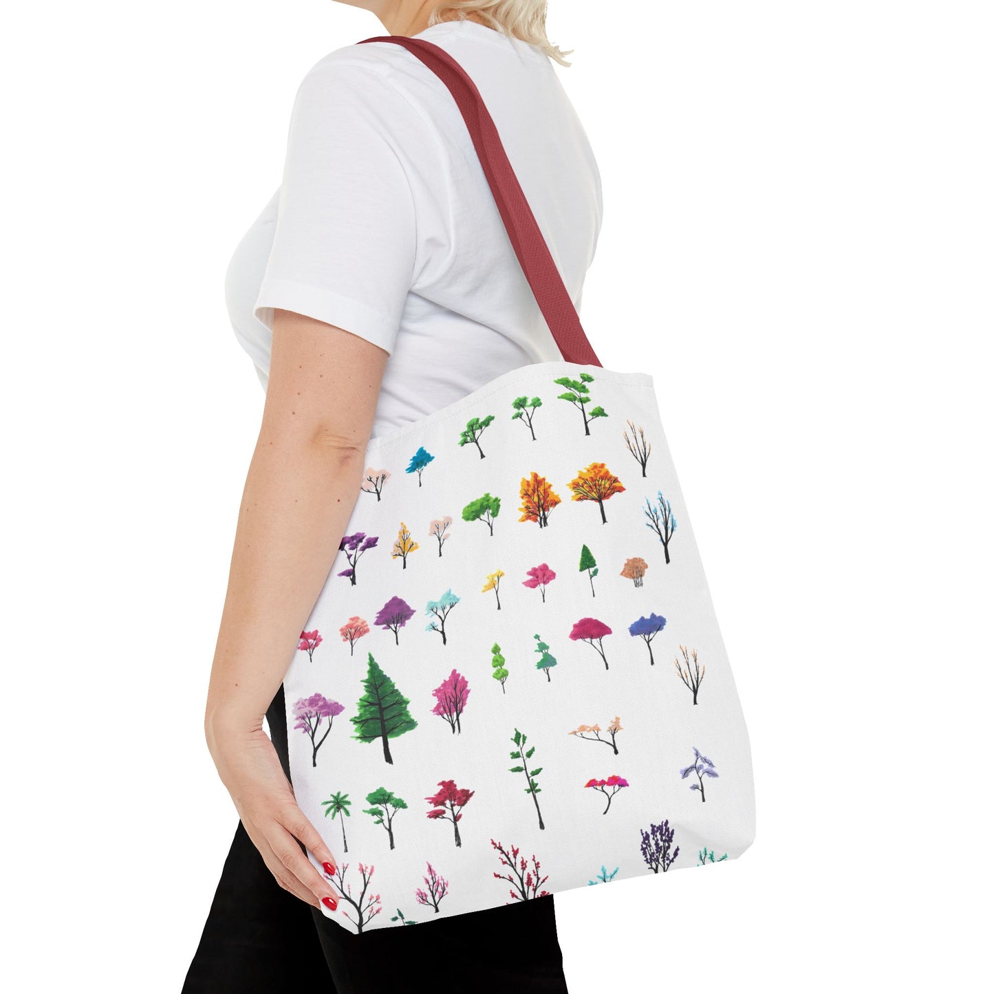 This is the Red 16" x 16" Study of Trees Tote with color matched handles by Lee Hansheng Studios. There are a variety of tree illustrations from blooming fruit trees to deciduous and evergreens. The trees are colored pinks, purples, greens, yellows, blues and oranges on a white background. The tote is over the shoulder of a short blonde haired woman who has a white tee and black pants. Her hand is on the tote and image only shows from the neck to upper thigh.