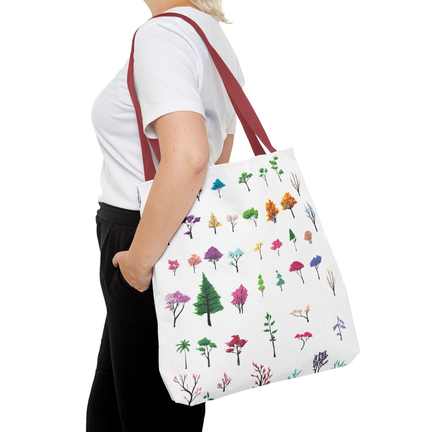 This is the Red 18" x 18" Study of Trees Tote with color matched handles by Lee Hansheng Studios. There are a variety of tree illustrations from blooming fruit trees to deciduous and evergreens. The trees are colored pinks, purples, greens, yellows, blues and oranges on a white background. The tote is over the shoulder of a short blonde haired woman who has a white tee and black pants. Her hand is in the pocket of the pants and image only shows from the neck to upper thigh.