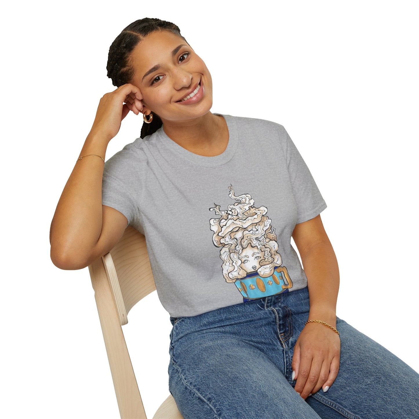 This is the Sport Grey Earl Grey Softstyle T-Shirt by Chris Foster Design. It comes in sizes XS-5XL. The illustration is of a gold, light blue and dark blue teacup with a tan, yellow and white steam. The steam is swirly and goes up and outwards. In the middle is a lady's face. A smiling lady is sitting on a light wood chair with the backrest to the left, elbow on the back rest, dark jeans, looking to the front and wearing the t-shirt.