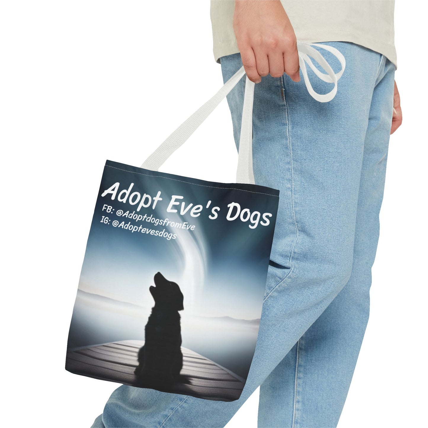 This is the White 13" x 13" Adopt Eve's Dogs Tote with color matched handles. This is an all around print tote with "Adopt Eve's Dogs" and socials on the top in white. The print is of a shadow of a golden retriever looking to the left on a pier towards water with mountains surrounding it.