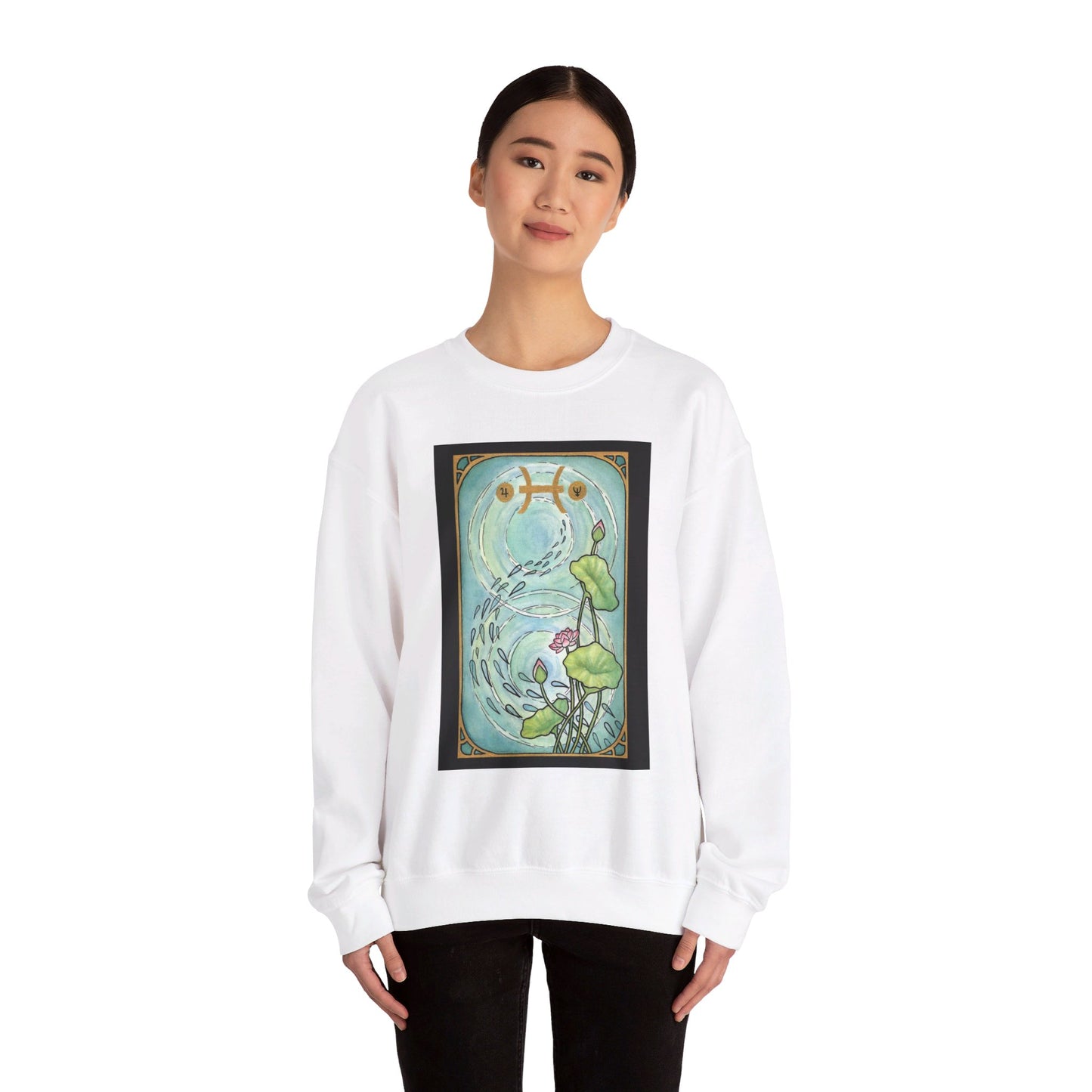 This is the White Pisces Sweatshirt by Chris Foster Design that comes in sizes S-3XL and illustration starts from the upper chest till below the belly button. Designed like a tarot card with gold border and pisces symbol. In the background a pond that has two circular ripples, the right side has the lily flowers with two green leaves, one blooming pink flower, two buds, and a green trail of seeds. A lady with a smile, black pants, hair tied and hands to the sides is wearing the sweatshirt.