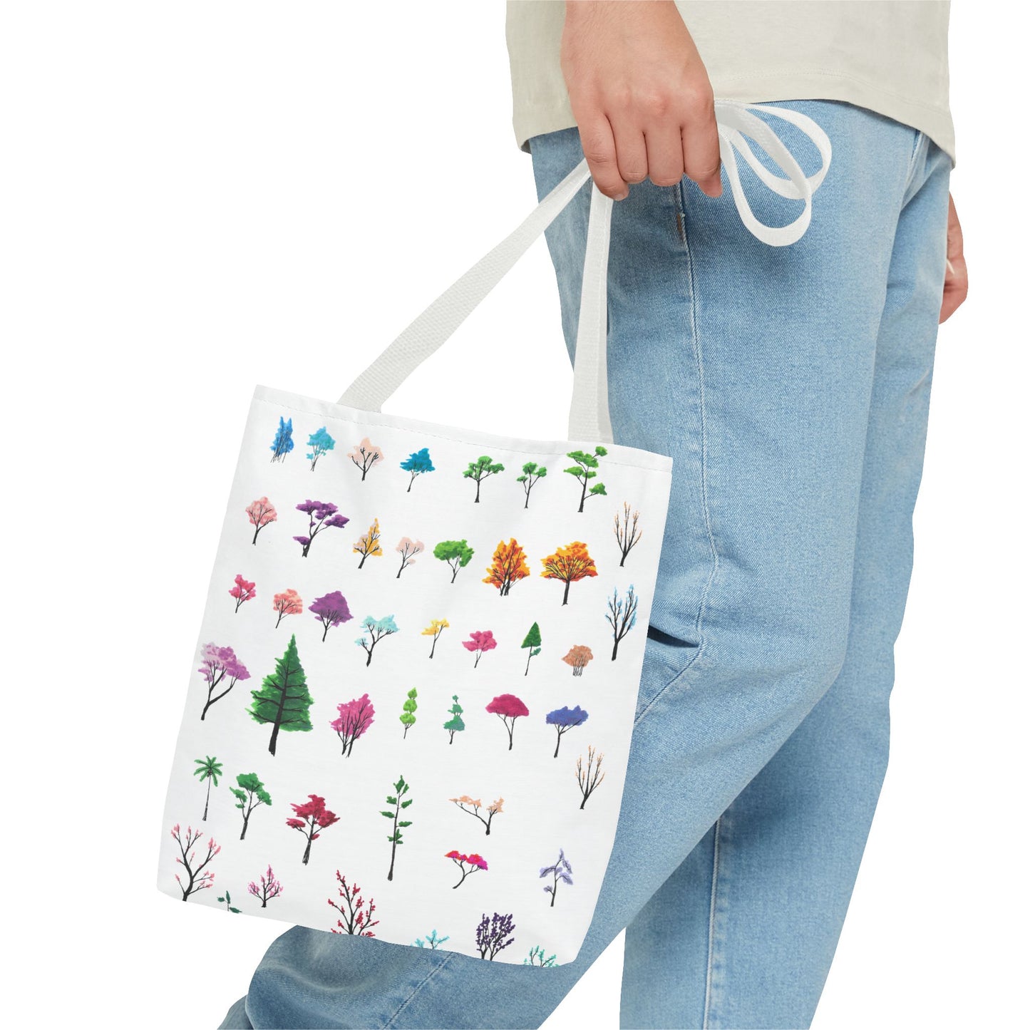 The White 13" x 13" Study of Trees Tote with color matched handles by Lee Hansheng Studios. There are a variety of tree illustrations from blooming fruit trees to deciduous and evergreens. The trees are colored pinks, purples, greens, yellows, blues and oranges on a white background tote. A man's hand with a beige tee and light- colored jeans is grabbing the handles from the hip down. The tote is against a white background.