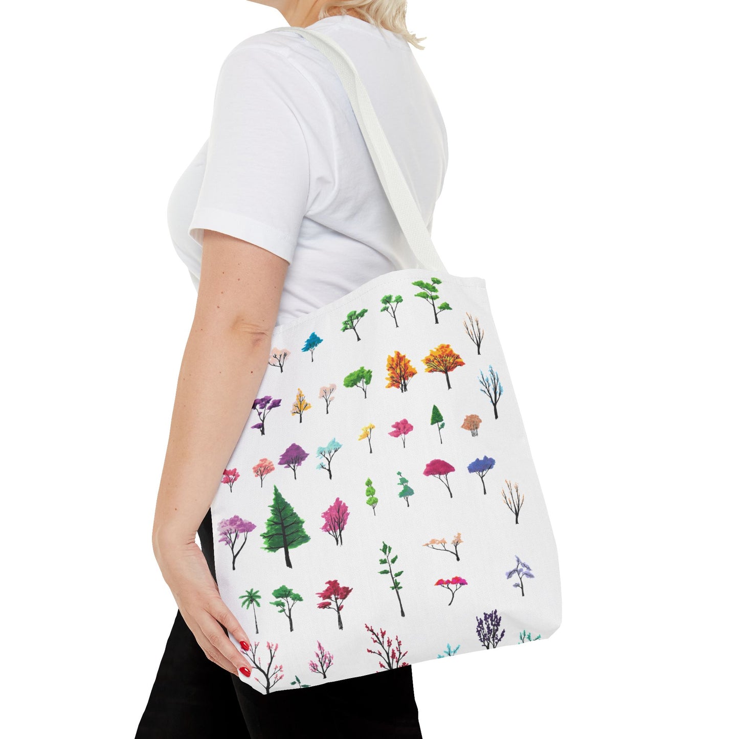 This is the White 16" x 16" Study of Trees Tote with color matched handles by Lee Hansheng Studios. There are a variety of tree illustrations from blooming fruit trees to deciduous and evergreens. The trees are colored pinks, purples, greens, yellows, blues and oranges on a white background. The tote is over the shoulder of a short blonde haired woman who has a white tee and black pants. Her hand is on the tote and image only shows from the neck to upper thigh.