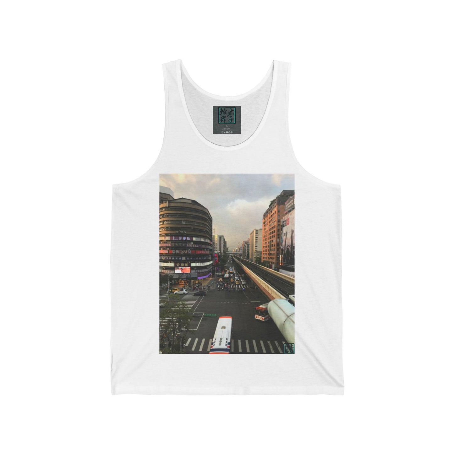 This is the White Taipei MRT Sunset Tank by Lee Hansheng Studios.This showcases the front of the tank.It is a rectangular image of Taipei.Circular brown building to the left,rectangular brown and white buildings to the right,two white/red buses pulling onto the road,overcast white,light red and grey skies,some trees to the right.It is the overall scenery from the looking across the road at higher ground.The studio logo on in the side of shirt,on top of gray label,size label is in white.