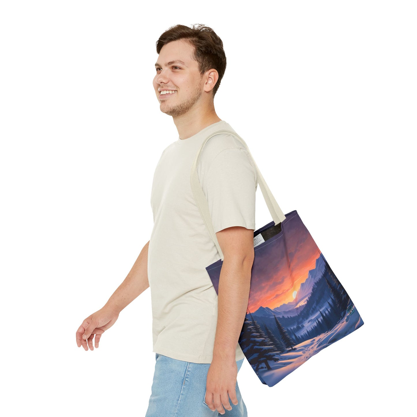 The Beige 13" x 13" Snow Valley Tote Bag has color matched handles. A man with a smile, short wavy brown hair,beige tee plus jeans with tote around their shoulder and walking towards the left against a white background.The design by Lee Hansheng Studios showcases a snowy hill/mountain area with large pine trees on both sides continuing into the horizon. The sun rises past the horizon consisting of yellow,orange,red hues illuminating onto wispy clouds,snowy field, mountains and dark green pine trees. 