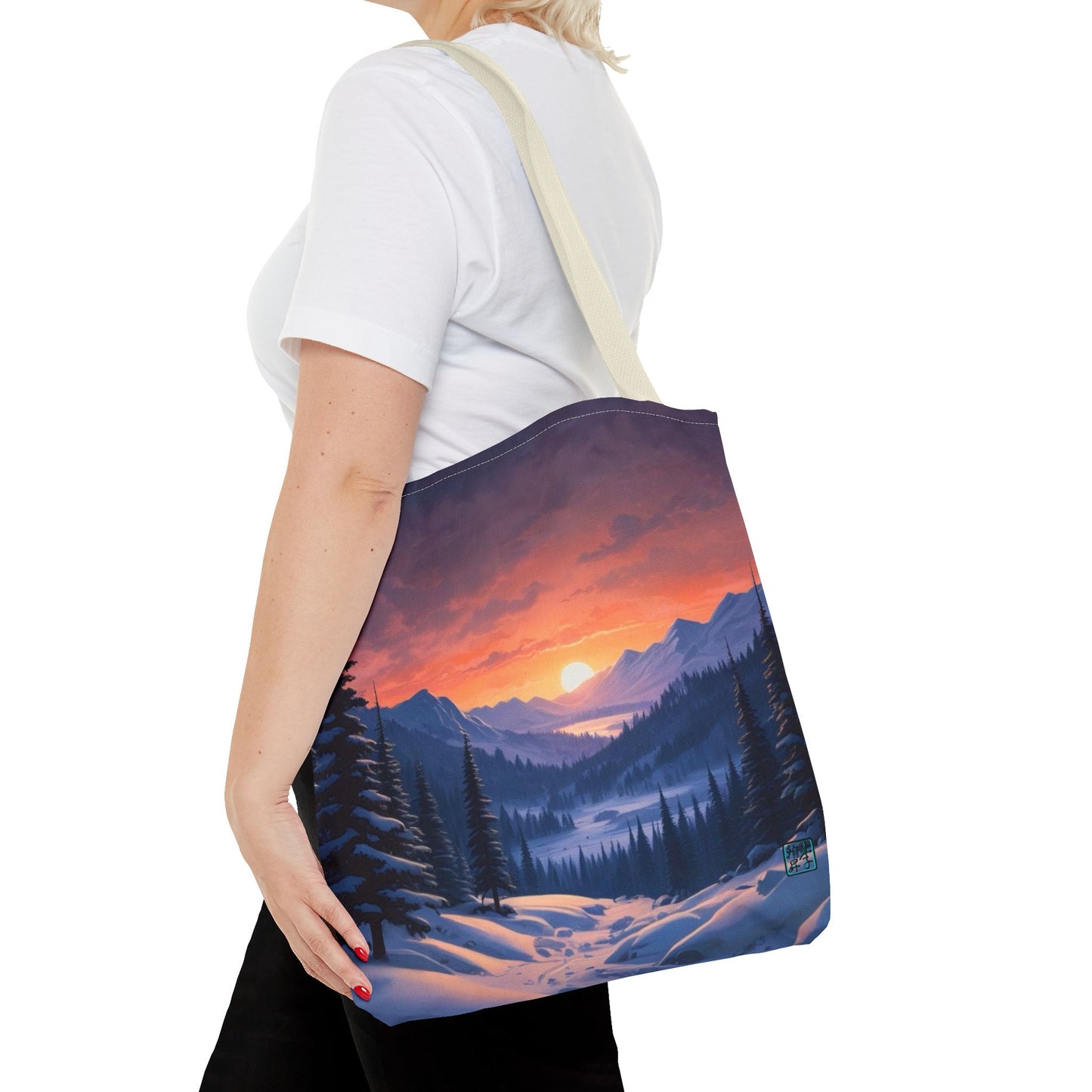 The Beige 16" x 16" Snow Valley Tote Bag has color matched handles. A lady with short blonde hair,white tee plus black pants with tote around their shoulder and hand in pocket against a white background.The design by Lee Hansheng Studios showcases a snowy hill/mountain area with large pine trees on both sides continuing into the horizon. The sun rises past the horizon consisting of yellow,orange,red hues illuminating onto wispy clouds,snowy field, mountains and dark green pine trees. 