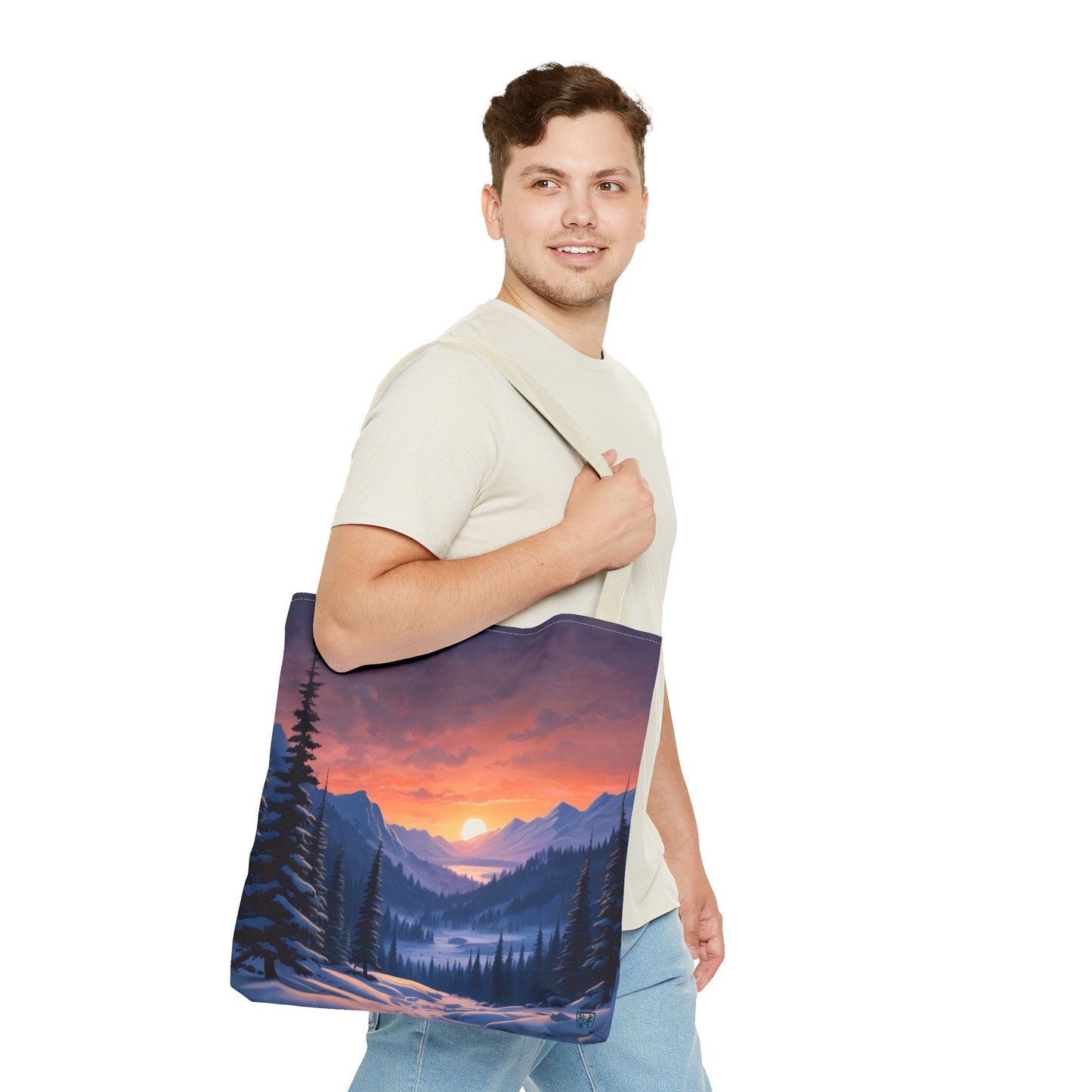 The Beige 16" x 16" Snow Valley Tote Bag has color matched handles. A man with a smile, short wavy brown hair,beige tee plus jeans with tote around their shoulder and walking to the right against a white background.The design by Lee Hansheng Studios showcases a snowy hill/mountain area with large pine trees on both sides continuing into the horizon. The sun rises past the horizon consisting of yellow,orange,red hues illuminating onto wispy clouds,snowy field, mountains and dark green pine trees. 