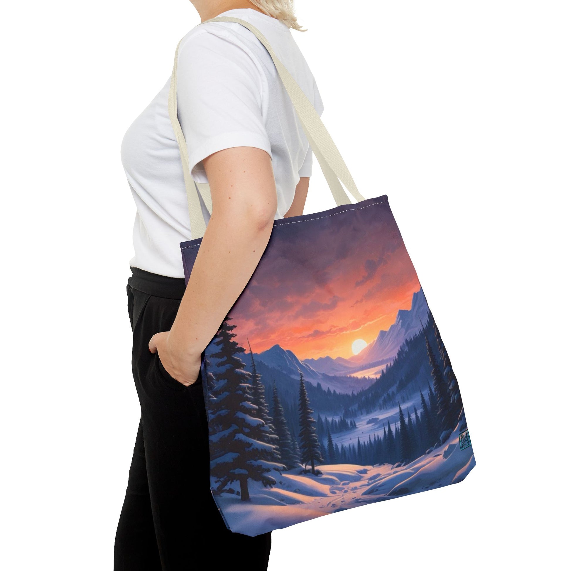 The Beige 18" x 18" Snow Valley Tote Bag has color matched handles. A lady with short blonde hair,white tee plus black pants with tote around their shoulder and hand in pocket against a white background.The design by Lee Hansheng Studios showcases a snowy hill/mountain area with large pine trees on both sides continuing into the horizon. The sun rises past the horizon consisting of yellow,orange,red hues illuminating onto wispy clouds,snowy field, mountains and dark green pine trees. 