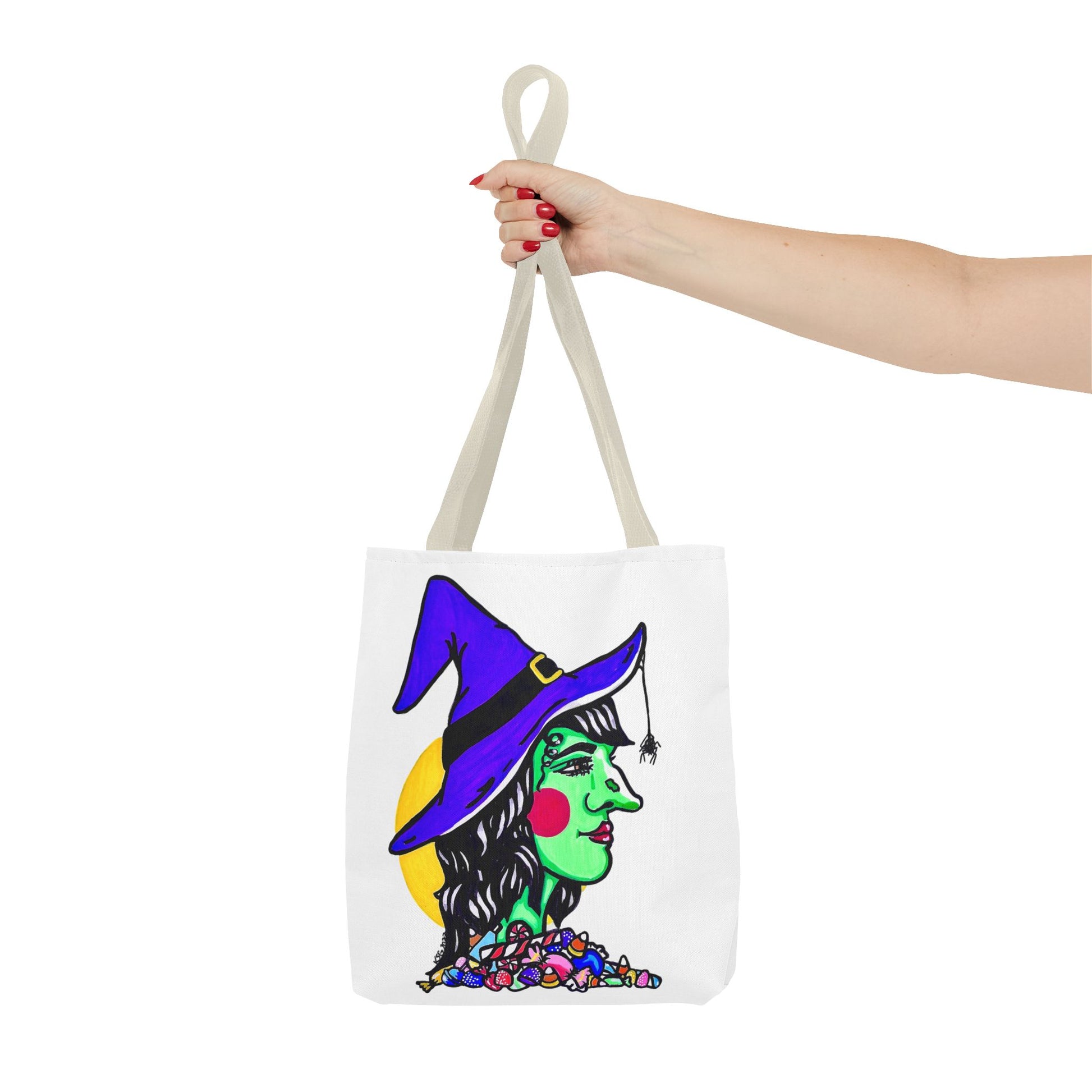 This is the Beige 13" x 13" Witch Tote Bag by Storm Garden Studio.The handles are color matched.It shows the side profile image of a witch.She is facing the left side.She has a purple witch hat with a black belt, yellow buckle, a spider crawling down the front, red rosy cheeks, red lips and assorted candy under the neck.Behind her is a bright yellow circle past her hair.A woman's hand with red nail polish is grabbing the handles. Her arm is outstretched to the middle. The tote is against a white background.