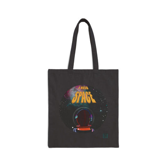 This is the Black 15" x 16" I NEED SPACE Canvas Tote Bag by Lee Hansheng Studios. This illustration is circular and has the print, "I NEED SPACE" in yellow, background of a galaxy and a person facing away towards the letters in a orange space suit. The colors are yellow, blue, red, pink and orange. On the bottom right of the tote is the studio's logo printed in black outlined in blue. This is an image of the tote from the front and against a white background.