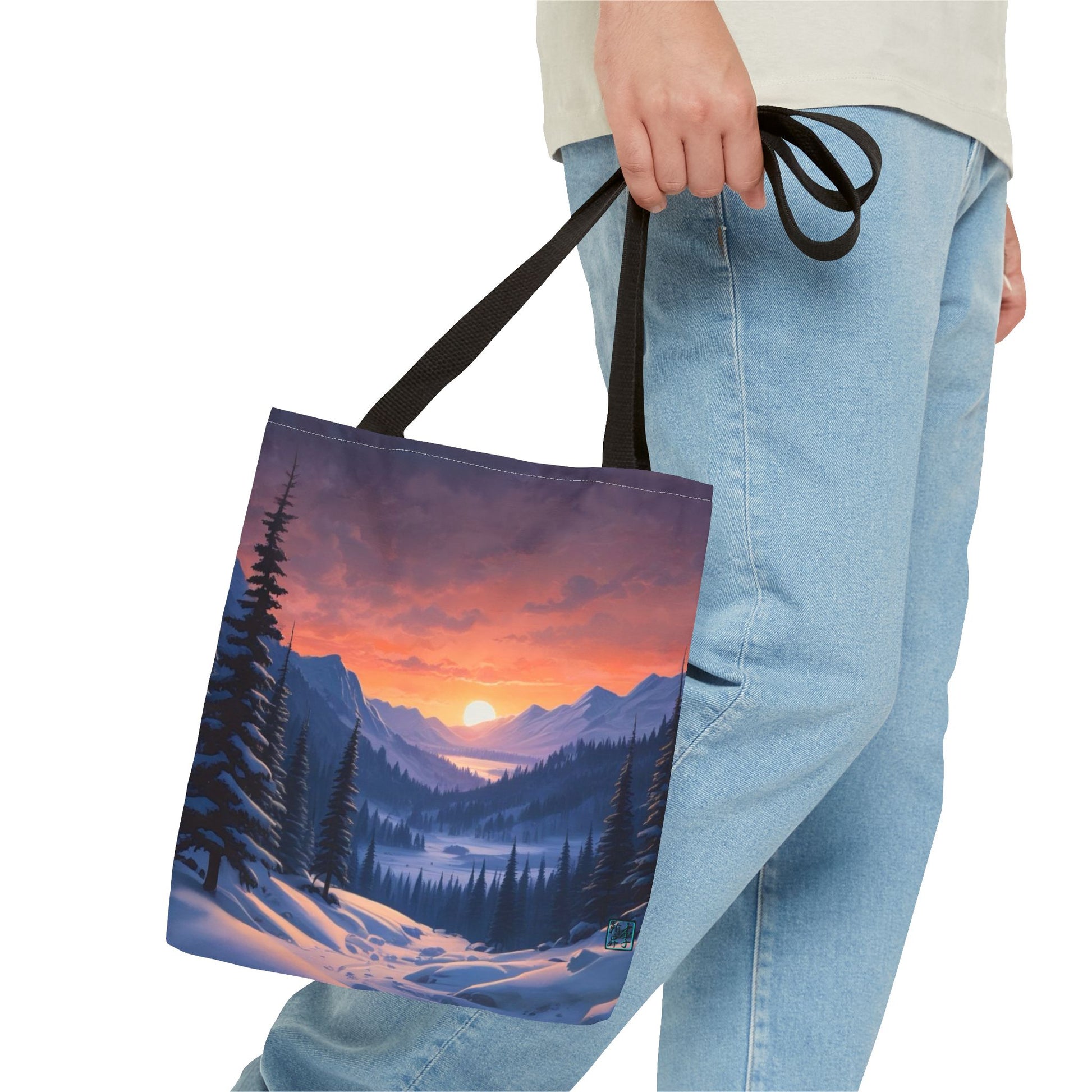 The Black 13" x 13" Snow Valley Tote Bag has color matched handles and all around print. A man's hand with a beige tee and light- colored jeans is grabbing the handles from the hip down. The tote is against a white background.The design by Lee Hansheng Studios showcases a snowy hill/mountain area with large pine trees on both sides continuing into the horizon. The sun rises past the horizon consisting of yellow,orange,red hues illuminating onto wispy clouds,snowy field, mountains and dark green pine trees. 