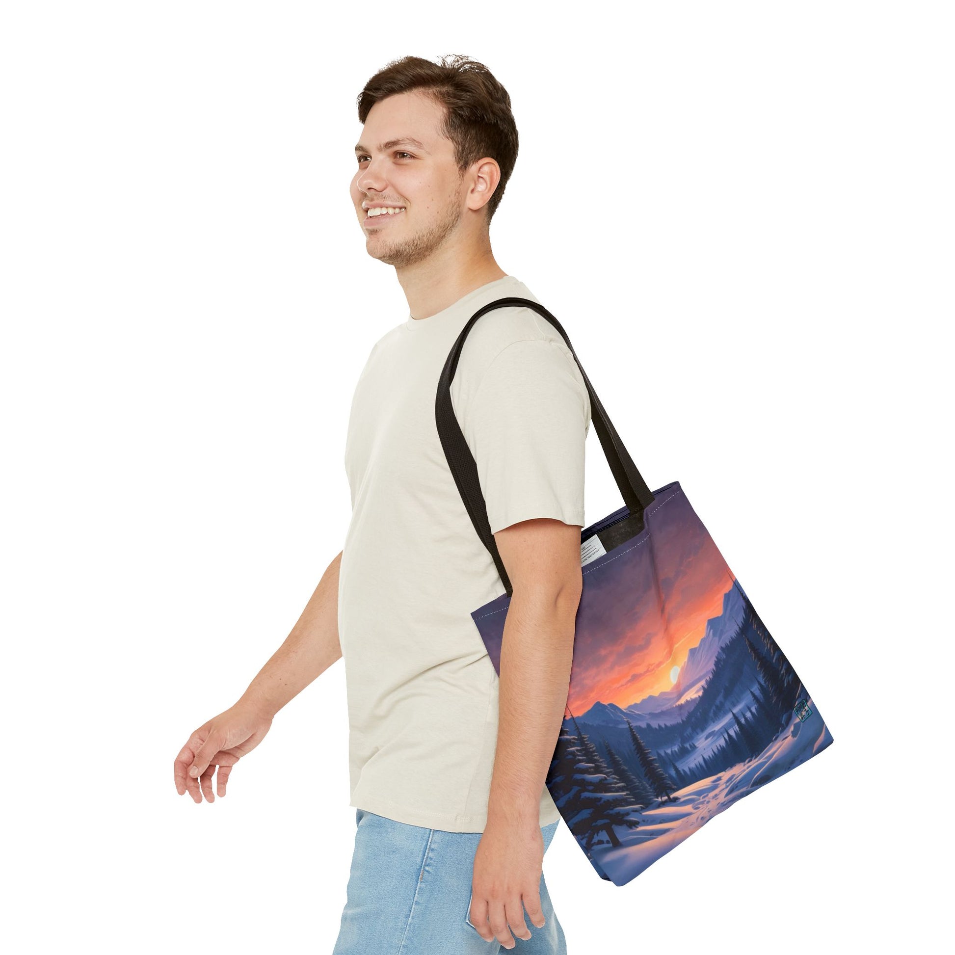 The Black 13" x 13" Snow Valley Tote Bag has color matched handles. A man with a smile, short wavy brown hair,beige tee plus jeans with tote around their shoulder and walking towards the left against a white background.The design by Lee Hansheng Studios showcases a snowy hill/mountain area with large pine trees on both sides continuing into the horizon. The sun rises past the horizon consisting of yellow,orange,red hues illuminating onto wispy clouds,snowy field, mountains and dark green pine trees. 