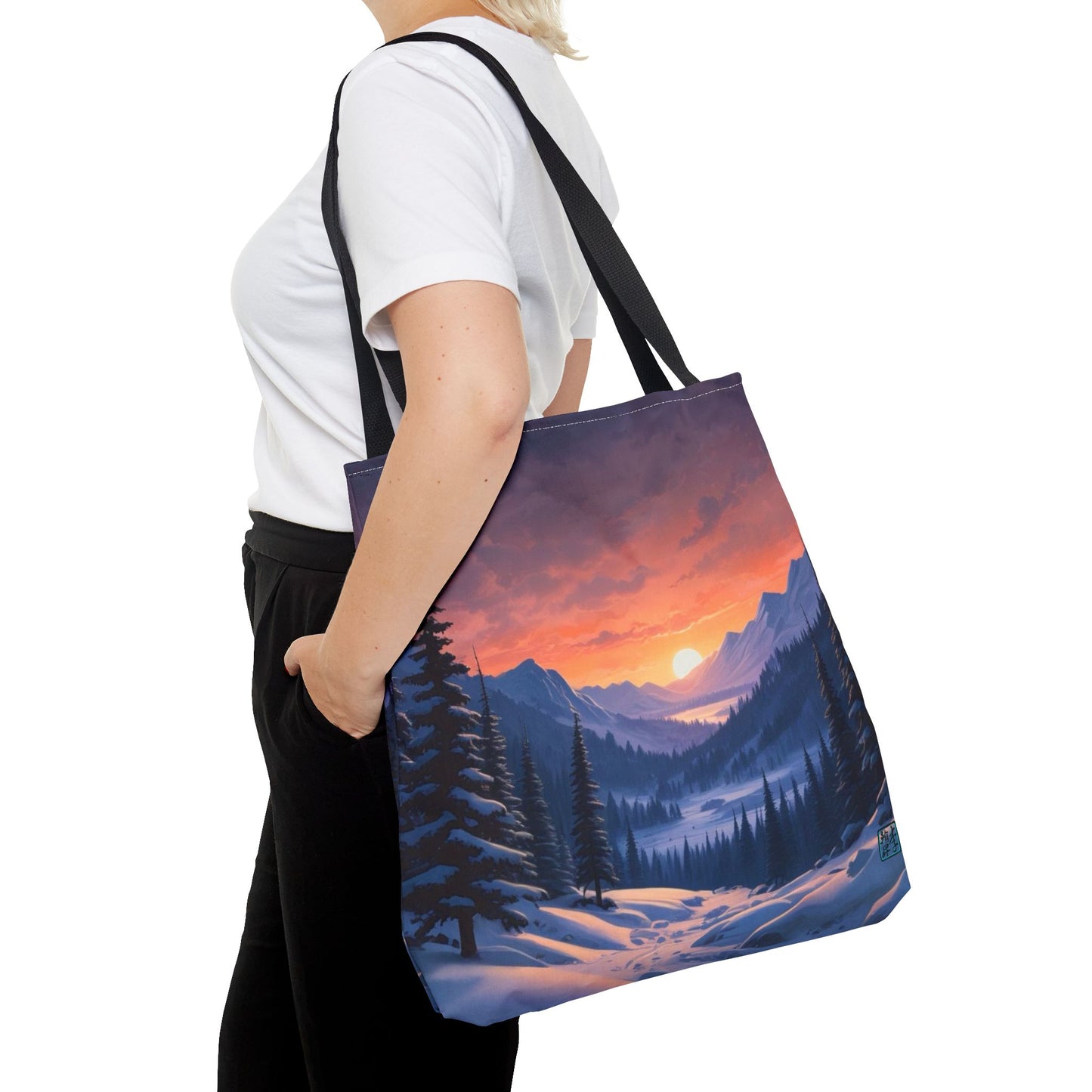 The Black 18" x 18" Snow Valley Tote Bag has color matched handles. A lady with short blonde hair,white tee plus black pants with tote around their shoulder and hand in pocket against a white background.The design by Lee Hansheng Studios showcases a snowy hill/mountain area with large pine trees on both sides continuing into the horizon. The sun rises past the horizon consisting of yellow,orange,red hues illuminating onto wispy clouds,snowy field, mountains and dark green pine trees. 