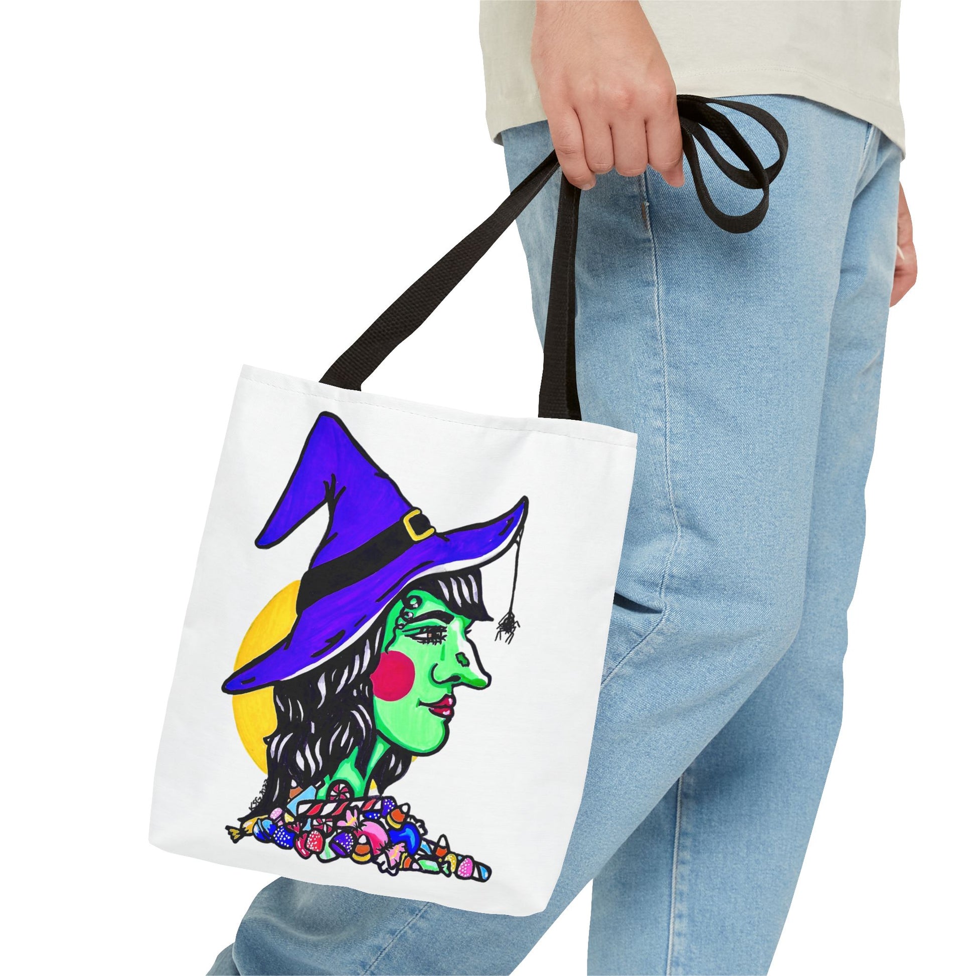 This is the Black 13" x 13" Witch Tote Bag by Storm Garden Studio. The handles are color matched. It shows the side profile of a witch. She has a purple witch hat, a black belt on hat, yellow buckle, a spider crawling down the front, red rosy cheeks, red lips and assorted candy under the neck. Behind her is a bright yellow circle past her hair. A man's hand with a beige tee and light- colored jeans is grabbing the handles from the hip down. The tote is against a white background.