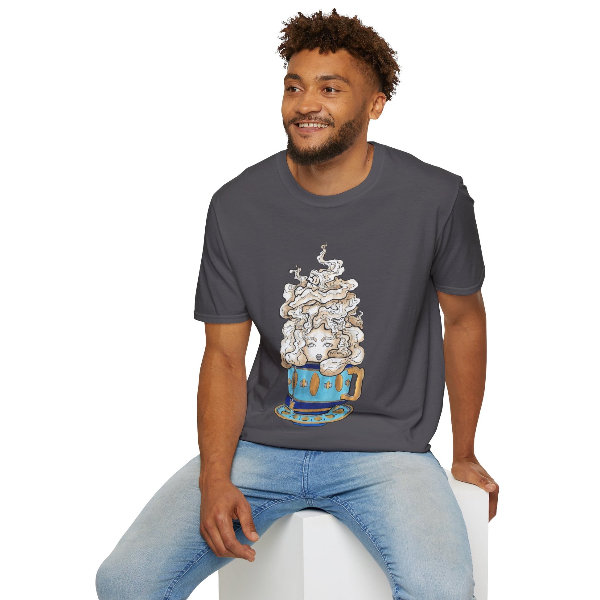 This is the Charcoal Earl Grey Softstyle T-Shirt by Chris Foster Design. It comes in sizes XS-5XL. The illustration is of a gold, light blue and dark blue teacup with a tan, yellow and white steam. The steam is swirly and goes up and outwards. In the middle is a lady's face. A smiling man sitting on a white podium with one hand on the back edge, light jeans, looking to the left and wearing the t-shirt. 