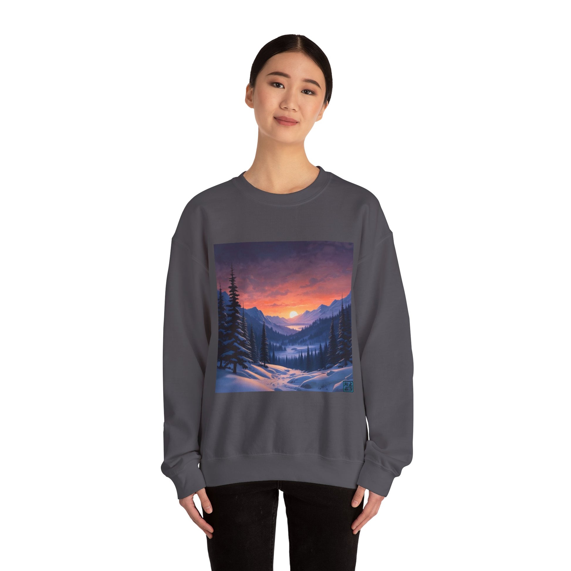 This is the Charcoal Snow Valley Sweatshirt that is a crewneck coming in S - 5XL sizes. It is worn by an Asian lady who has black hair tied in a bun, black pants and is standing against a white background with a smile. This design is by Lee Hansheng Studios and showcases a snowy hill/mountain area with large pine trees on both sides continuing into the horizon. The sun is rising past the horizon and consist of yellow, orange, red hues which is illuminated onto the clouds, snowy field, mountains and trees. 