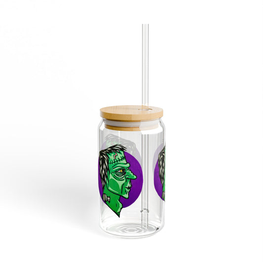 This is the 16oz Frankensteins Monster Sipper Glass with light colored bamboo lid and with straw slightly to the right by Storm Garden Studio. It is a side profile illustration of Frankenstein printed all around. He is facing the right side, a scar across the forehead, orange/yellow scar on the top of the forehead and a silver screw. He is all over green with shading on chin, cheeks and highbones. It is against a white background.