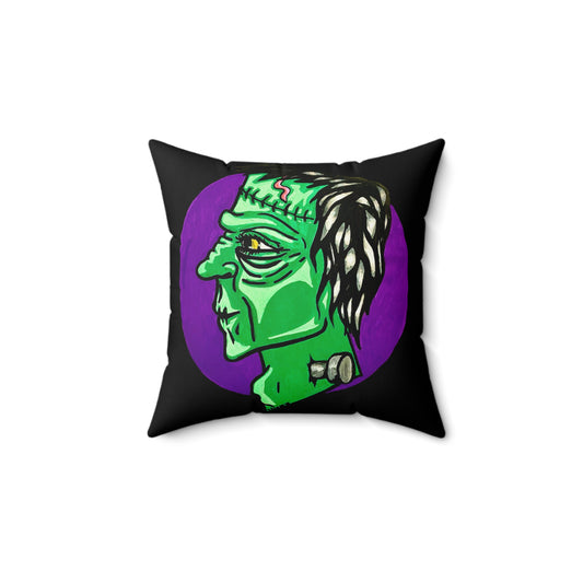 This is the 14" x 14" Frankensteins Monster Spun Polyester Square Pillow by Storm Garden Studio. The pillow overall is black and the illustration are on both sides. This showcases the back of the pillow. It is Frankenstein's side profile illustration. He is facing the right side, a scar across the forehead, orange/yellow scar on the top of the forehead and a silver screw. He is all over green with shading on chin, cheeks and highbones. It is against a white background.