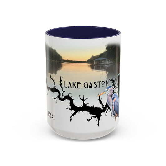 This is the 15oz Navy Lake Gaston Mug. It is an illustration by Lee Hansheng Studios. The picture is showing the front side of the mug. The inside of mug are color matched too. The mug is all white except for the illustration and handle. The illustration shows the lake on a horizon, the words "Lake Gaston", a black branch, and a blue heron on the right. The colors are orange, blue and green for the landscape. The mug is against a white background in the picture. 